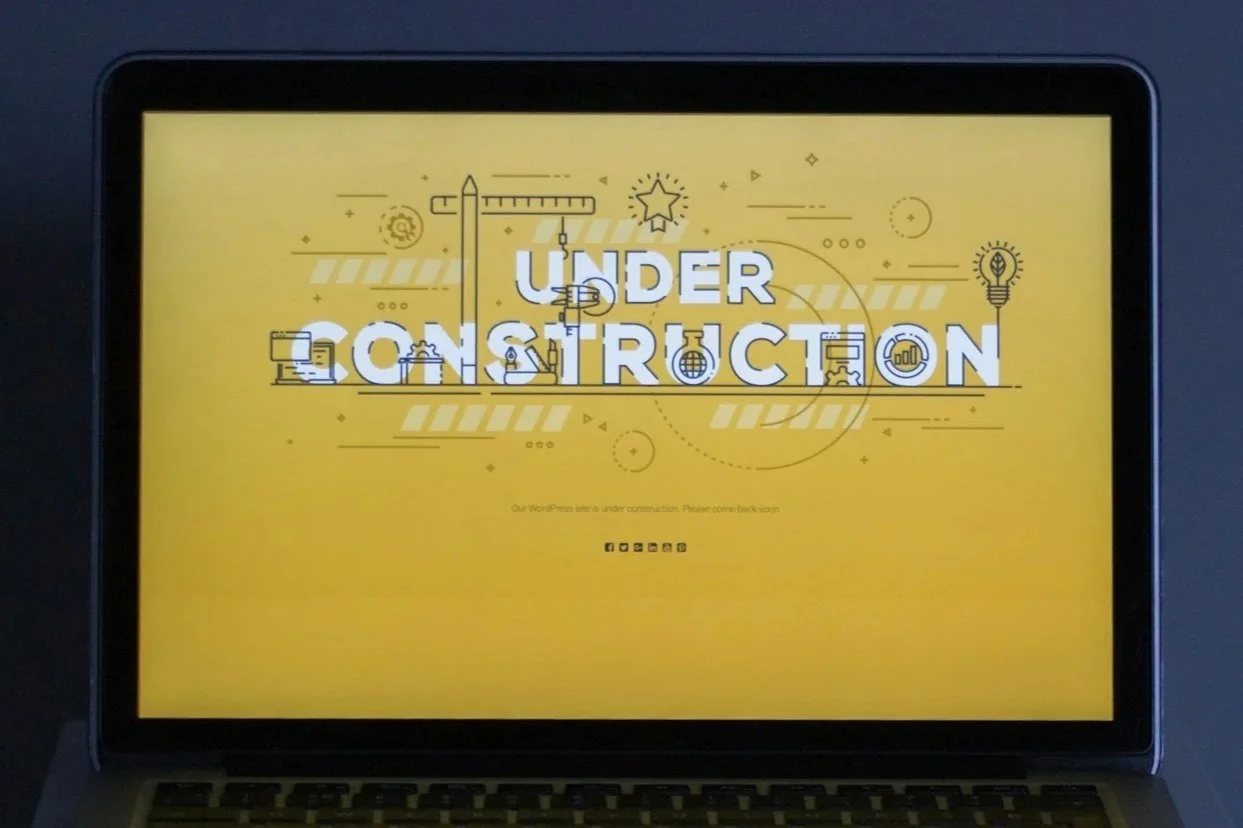 Laptop screen displaying a yellow graphic with construction tools and icons, and the text 'Under Construction'