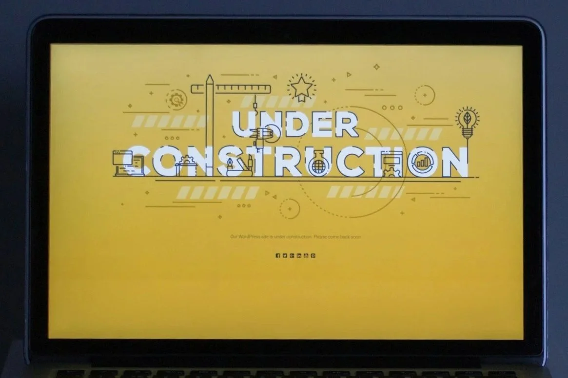 Computer screen displaying a yellow background with the text 'UNDER CONSTRUCTION' and construction-themed icons like a crane and light bulb, indicating the website is temporarily unavailable.