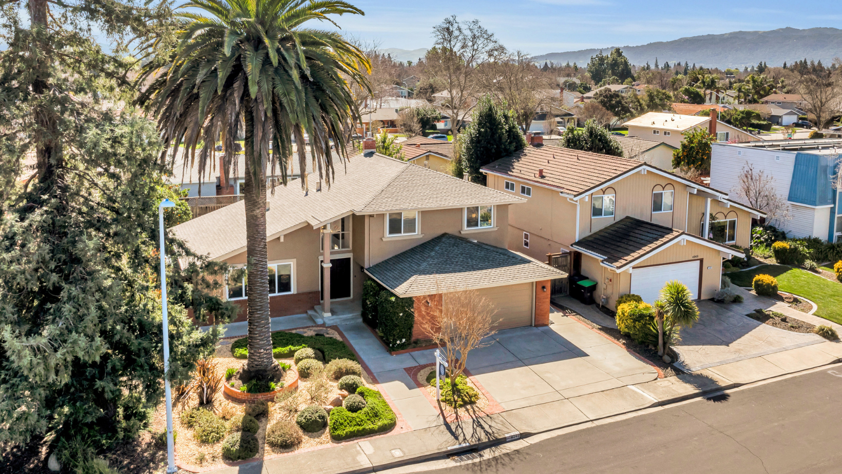 A two story home on Rockingham Drive, in the Pleasanton Meadows neighborhood of Pleasanton, California, huge palm tree in the front yard and views of mountain behind the home