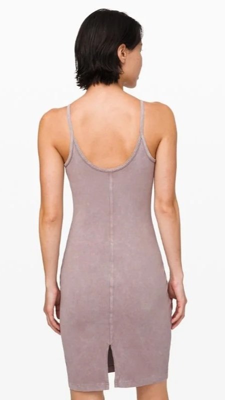 Back view of a woman in a fitted, sleeveless, light purple dress with a small slit at the bottom.