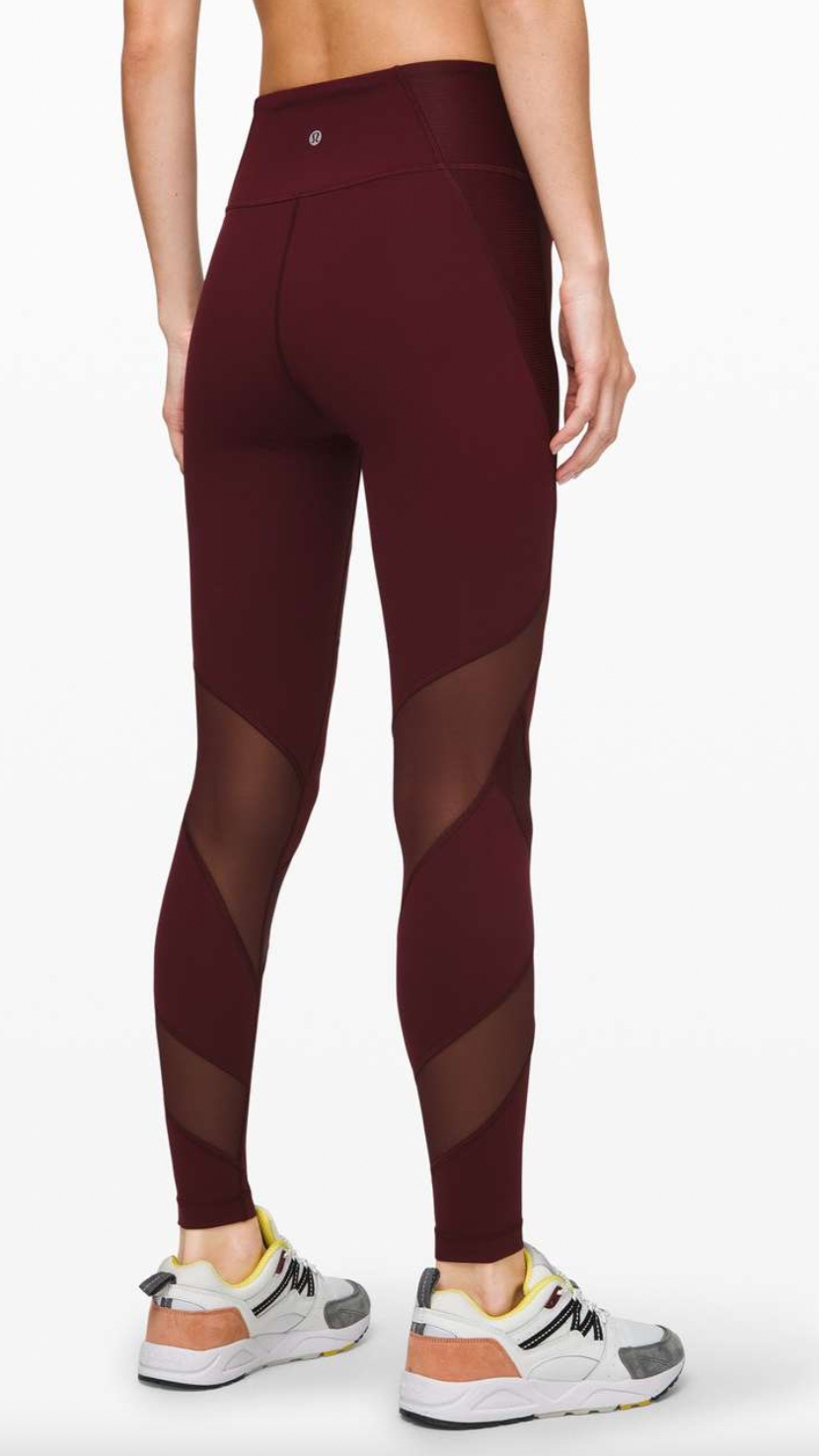 Back view of a woman wearing maroon leggings with sheer panels and a high waistband, paired with white running shoes with yellow and gray accents.