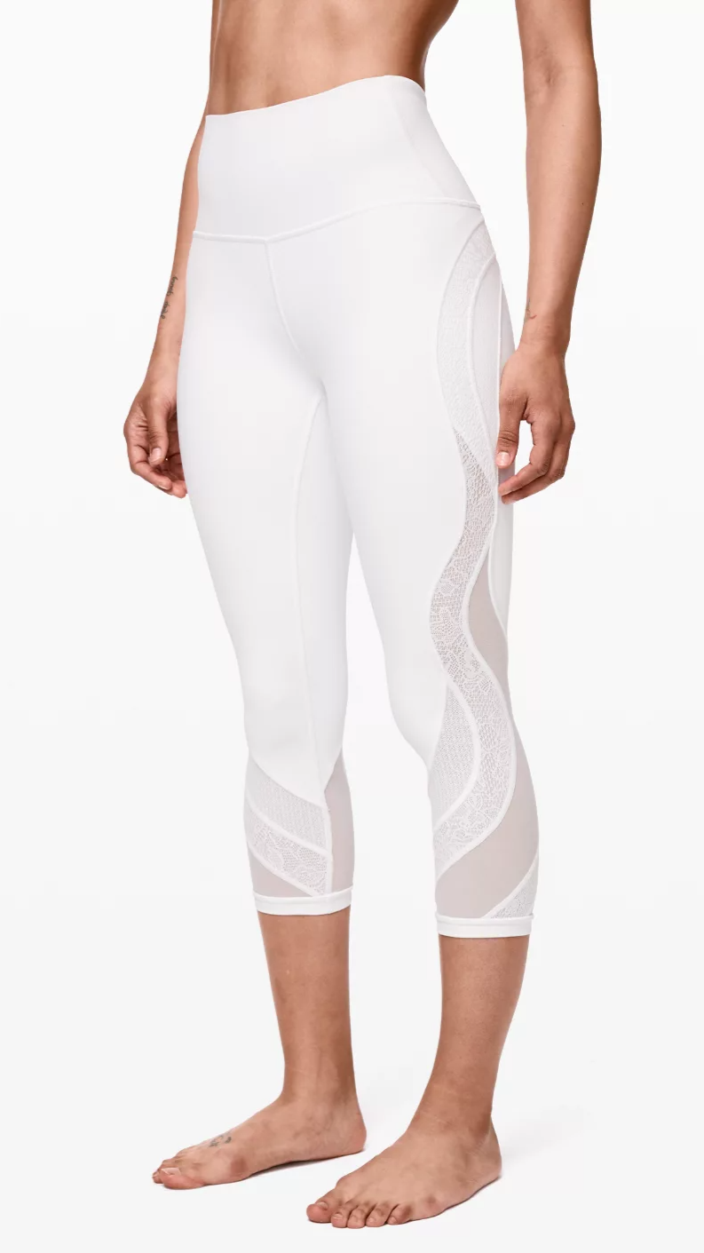 Close-up of a person wearing high-waisted white athletic leggings with mesh and patterned detailing on the sides.