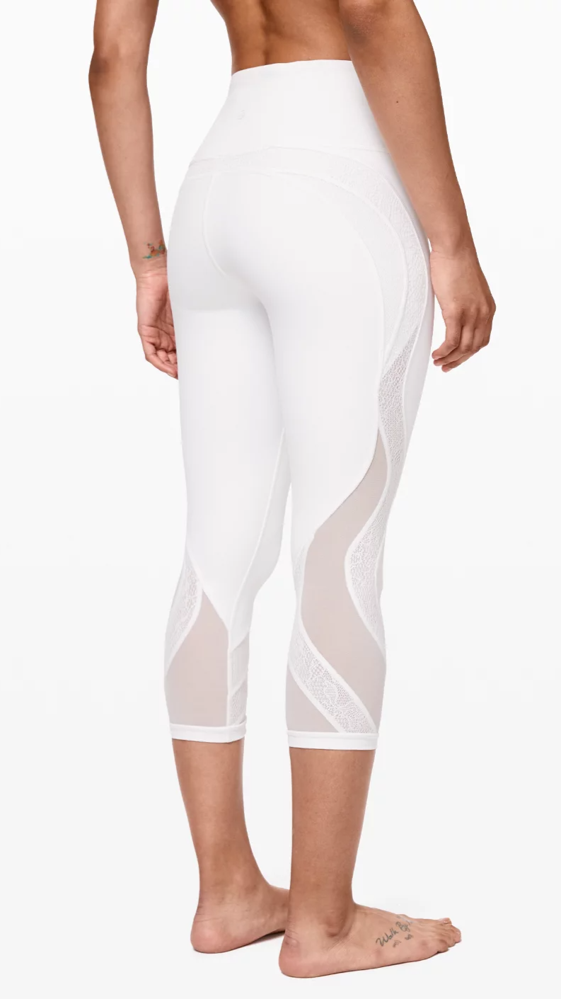 Back view of a person wearing white athletic leggings with mesh and lace details, barefoot, standing against a plain background.
