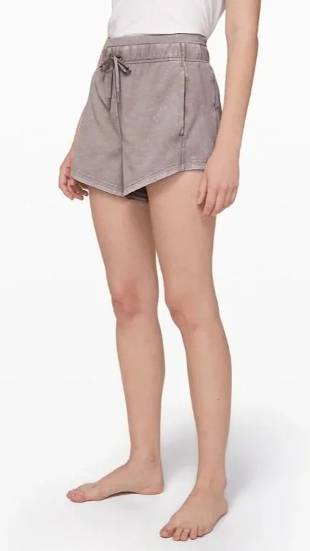 A woman wearing a white top and purple shorts standing barefoot against a white background.