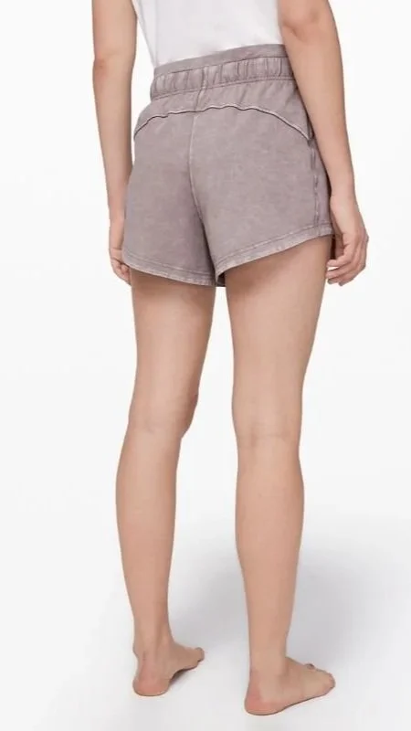 A person wearing gray shorts and a white top, standing barefoot against a white background.