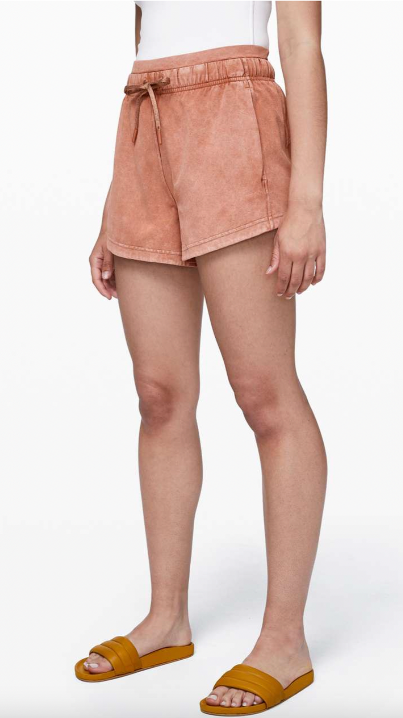 Person wearing peach-colored shorts, a white top, and yellow slide sandals against a plain white background.