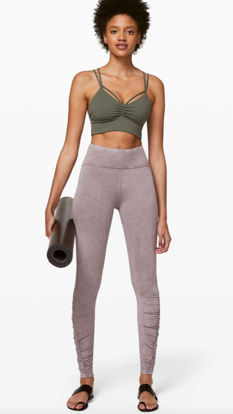 Woman in green sports bra and light pink leggings holding yoga mat