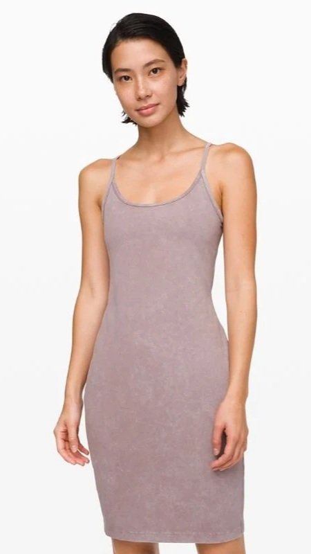 Woman wearing a light purple slip dress with thin straps, standing against a plain white background.