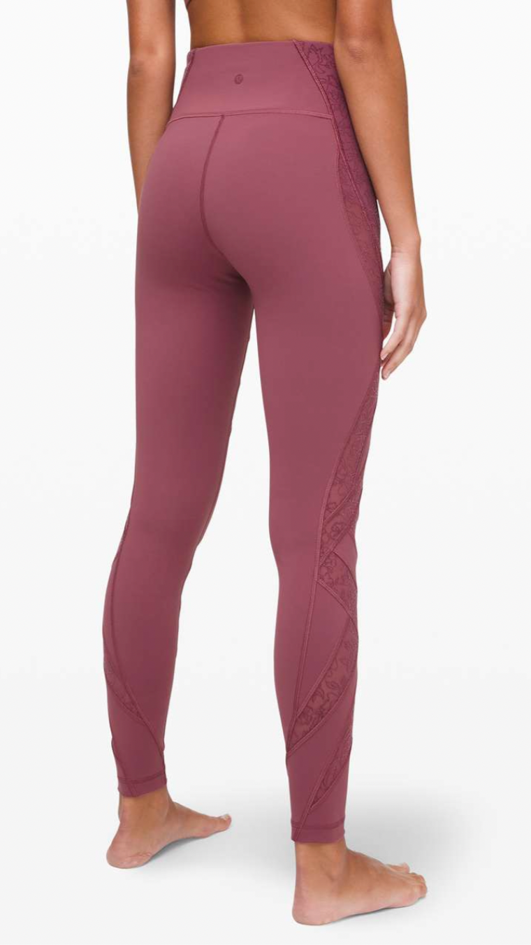Back view of a woman wearing high-waisted maroon athletic leggings with patterned side panels, standing barefoot on a white background.