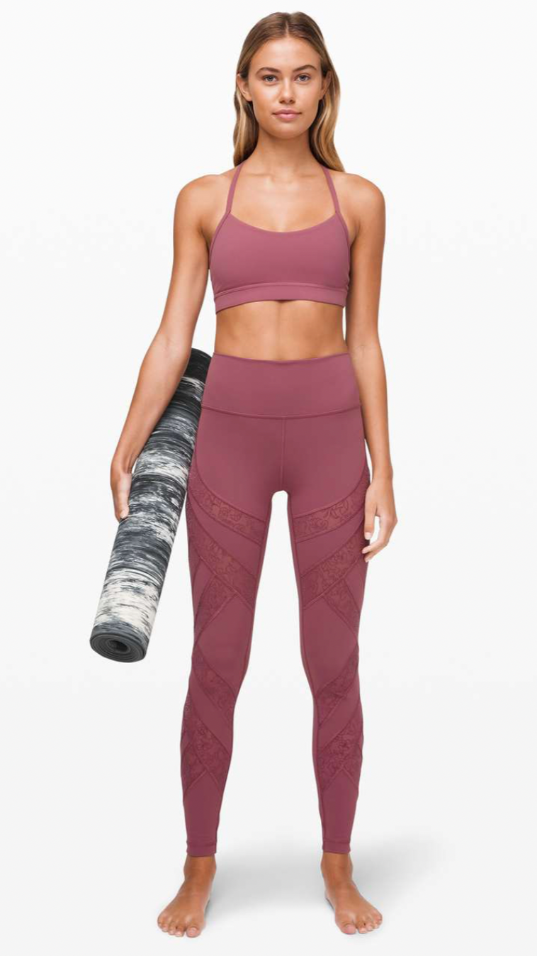 Young woman in pink athletic wear holding a rolled yoga mat on a white background.
