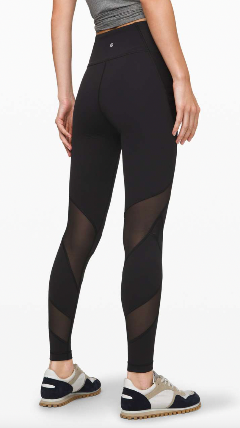 Back view of a woman wearing black athletic leggings with mesh panels, a gray sports bra, and running shoes.