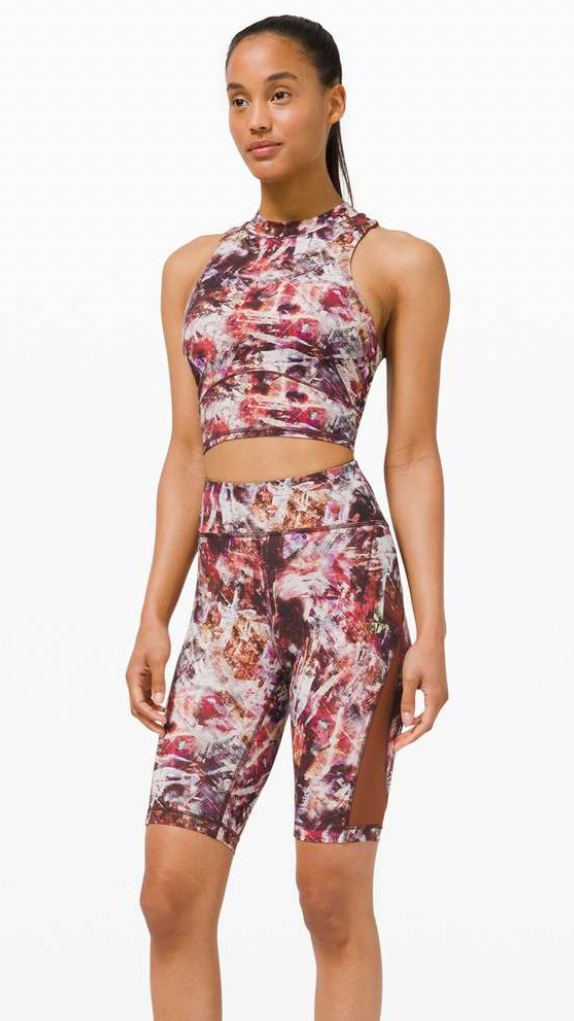 Young woman wearing colorful patterned athletic crop top and matching shorts with side slits, standing against a white background.