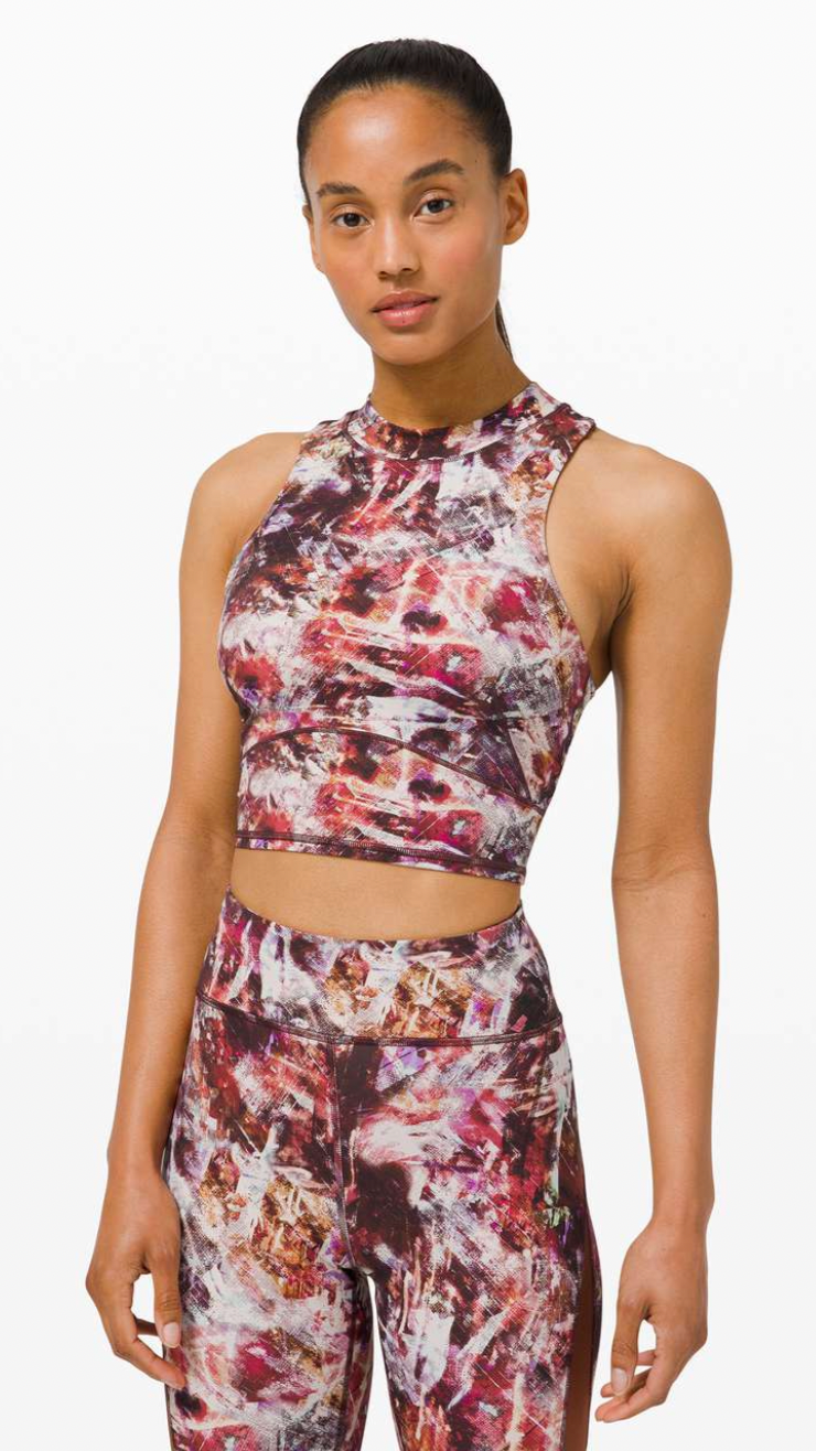 Woman wearing a sleeveless high-neck crop top and matching leggings with an abstract red, pink, and white pattern.