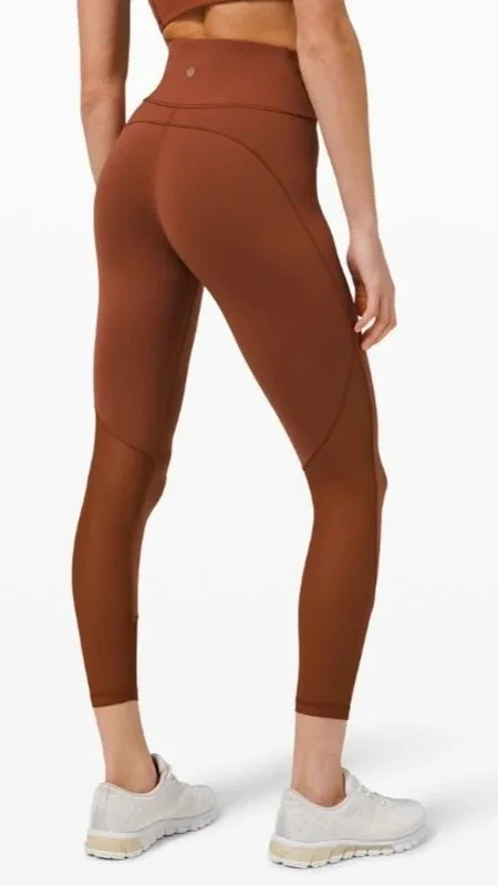 Back view of a woman wearing brown high-waisted athletic leggings and white running shoes.