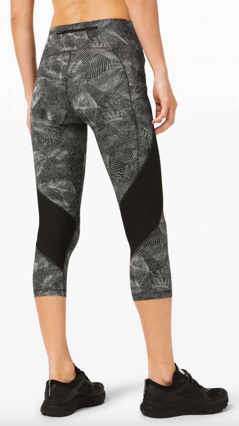 A person wearing black and gray patterned athletic capri leggings and black sneakers, standing against a white background.