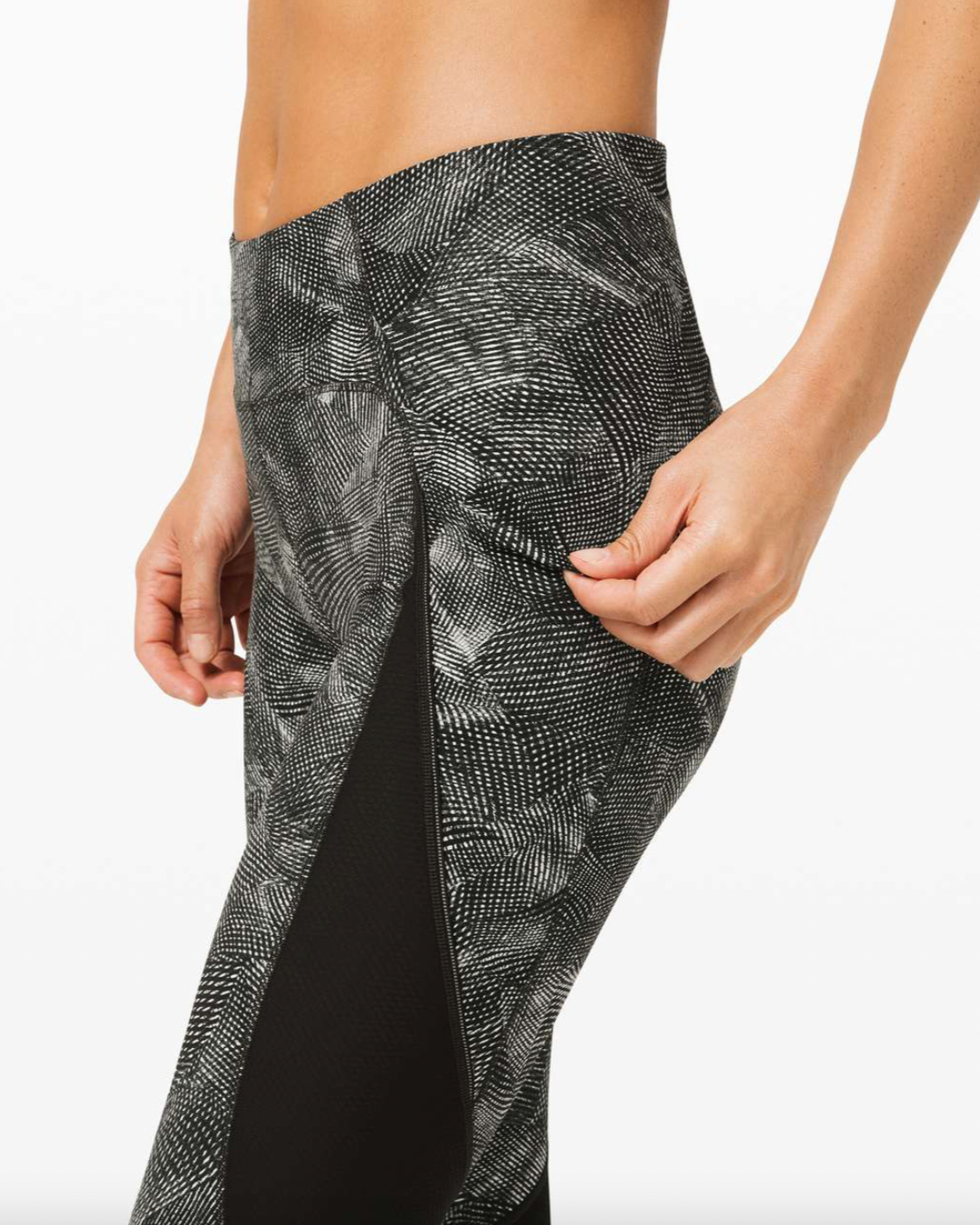 Close-up of a person's waist and hand, wearing black and white patterned athletic leggings with a slit on the side.