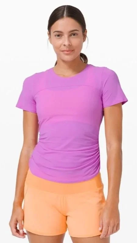 A young woman wearing a purple t-shirt and orange shorts, standing against a plain white background.