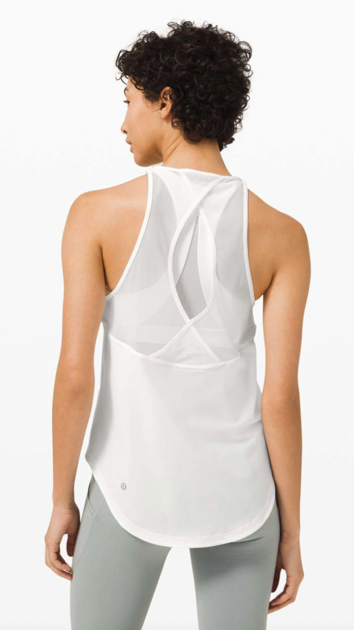 A woman with curly short hair wearing a sleeveless white athletic top with a unique back design, standing against a plain white background.