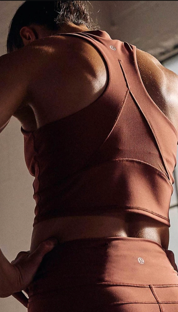 A person wearing a rust-colored sports bra and matching high-waisted athletic shorts, standing with one hand on their hip, captured from the back. The image is divided, with the other half showing a black-and-white photo of a person hanging upside do