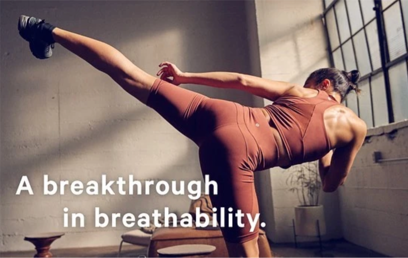 A woman in athletic clothing performing a yoga pose in a bright room with large windows, with the text 'A breakthrough in breathability.'