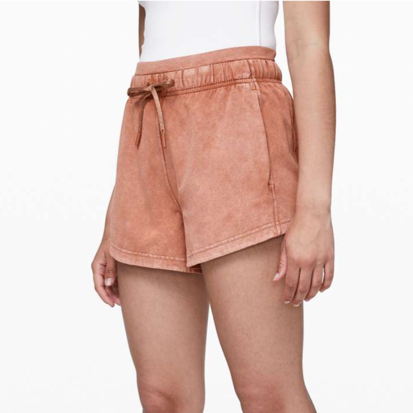 Woman wearing coral-colored shorts and mustard yellow sandals, cropped from waist to feet.