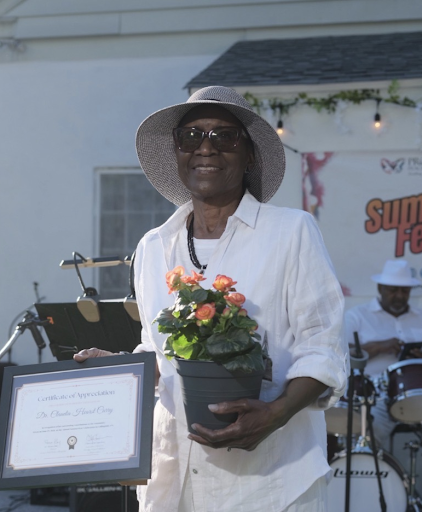 Curry poses in an open white button down holding the certification in one hand and a pot of orange flowers in the other.
