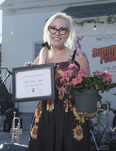 Medium full shot Jetter smiling holding the certificate in one hand and a pot of pink flowers in the other hand.