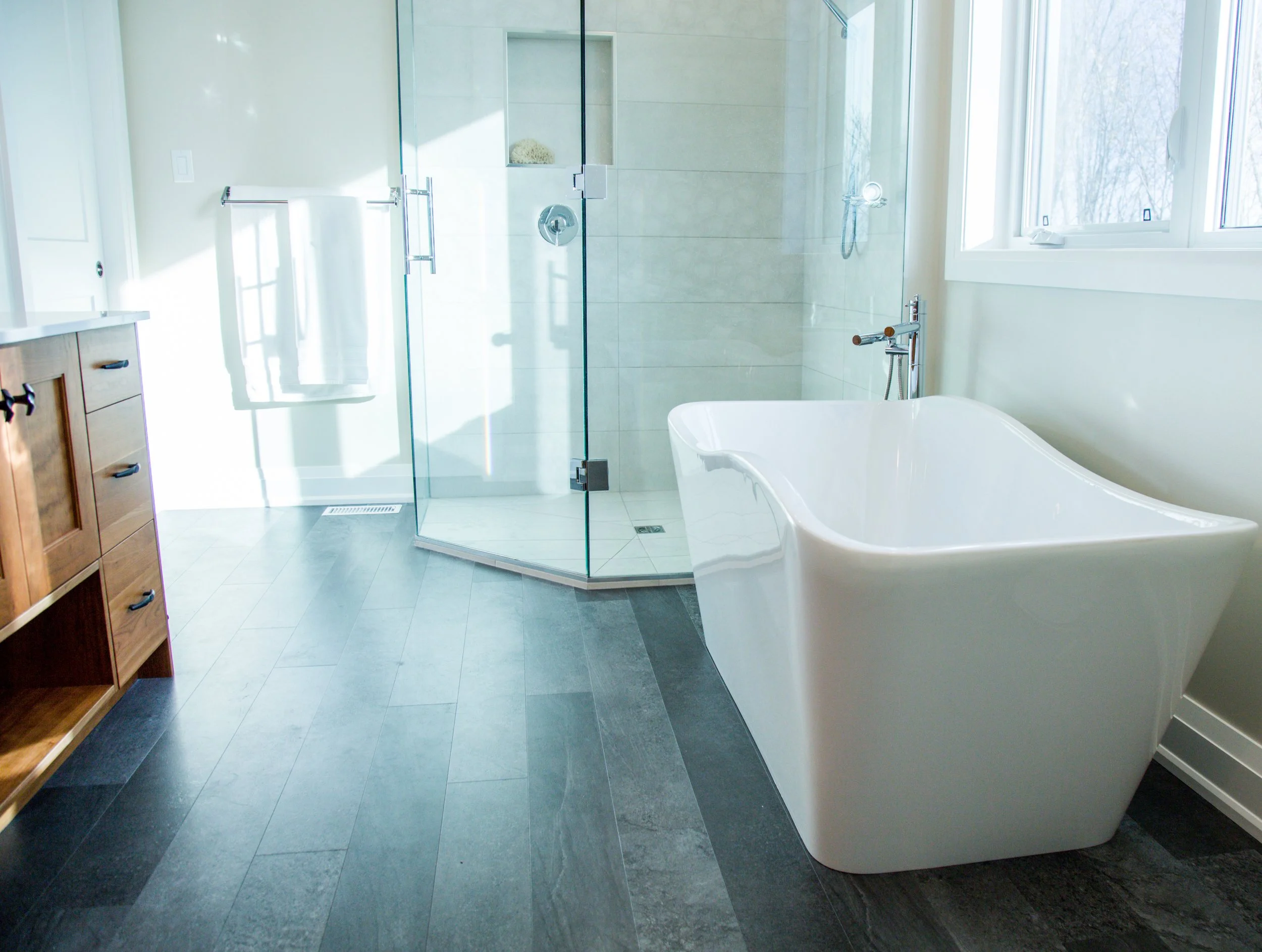 Modern bathroom featuring a glass walk-in shower, a white freestanding bathtub, and wooden cabinetry with a towel bar.