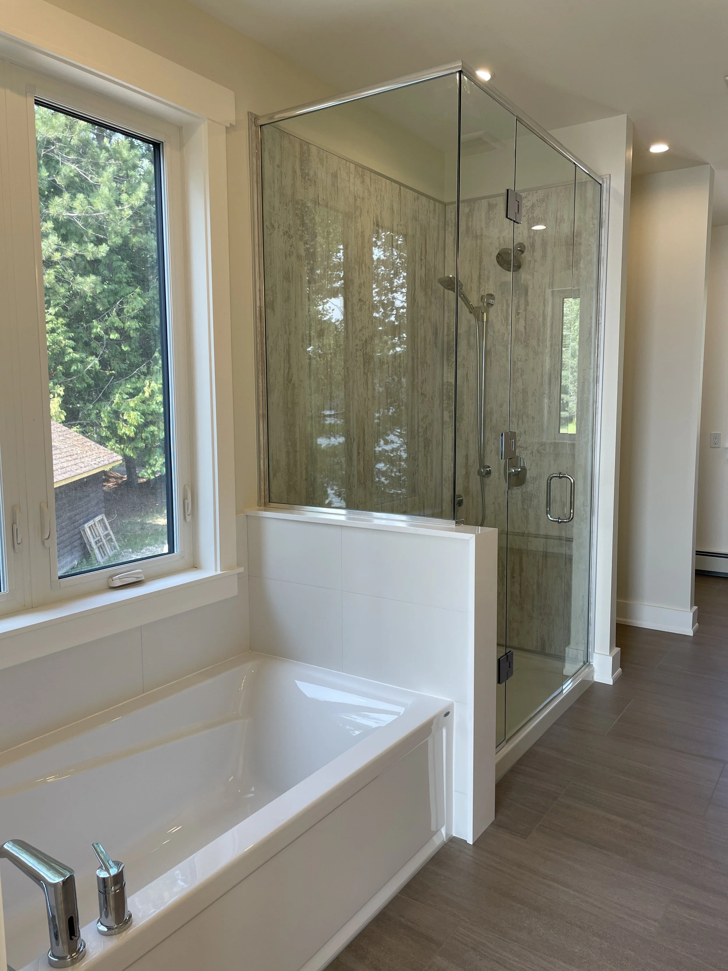 Bathroom featuring a bathtub next to a window and a glass-enclosed shower with beige tiled walls.