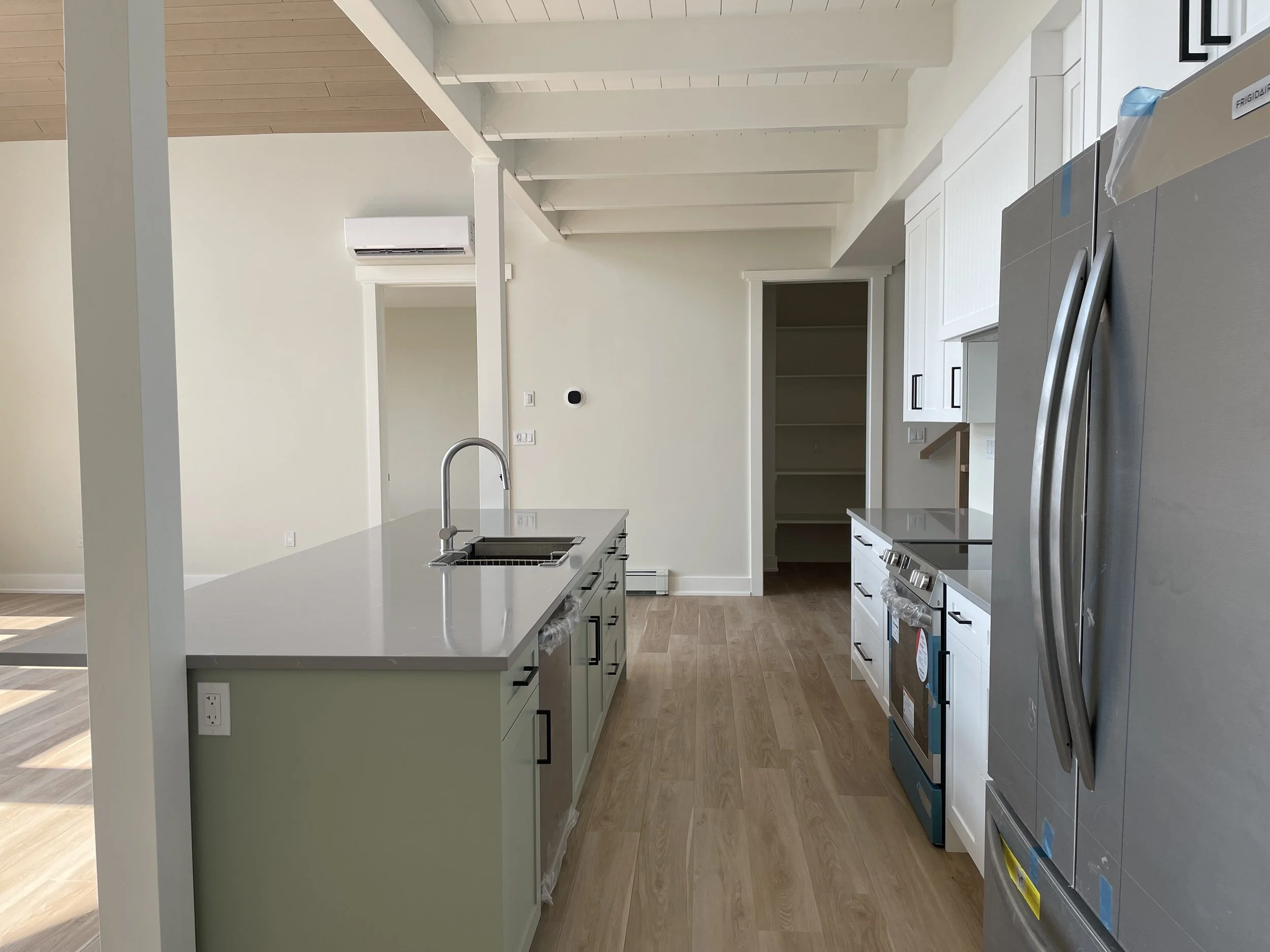 Empty kitchen with white cabinets, stainless steel appliances, a large kitchen island with a sink, and open shelving.