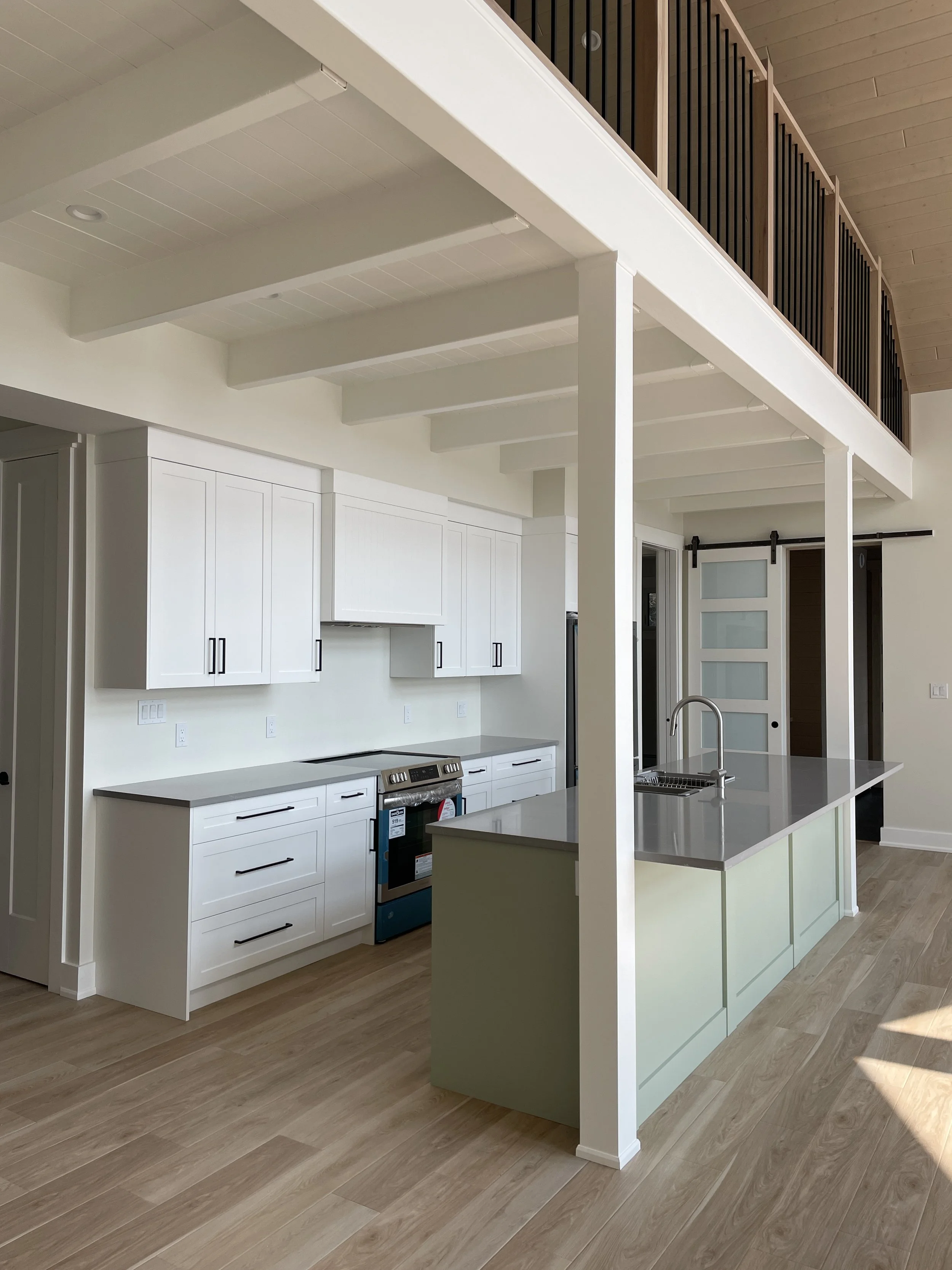 Modern kitchen with white cabinets, a kitchen island with a sink, light wood flooring, and a sliding barn door.
