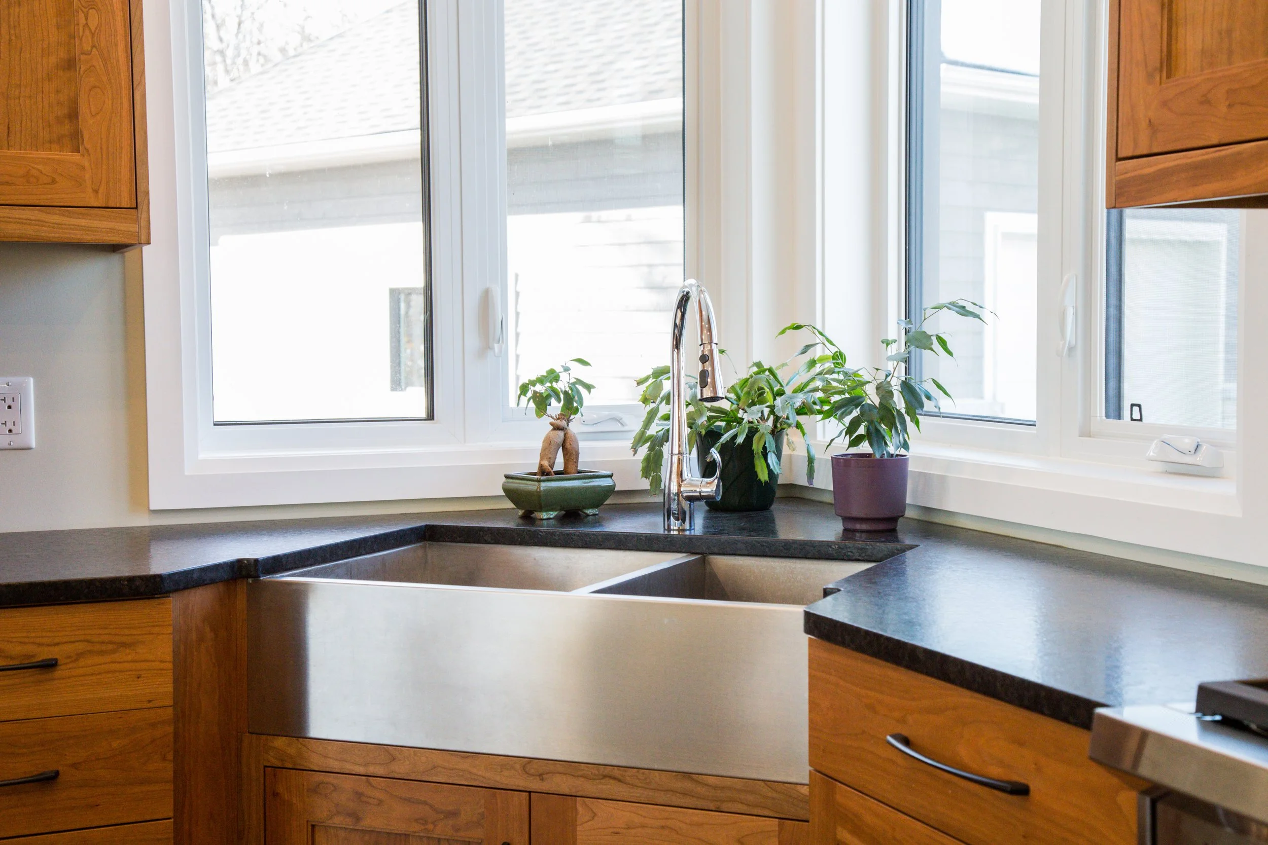 Kitchen sink area with a window above and potted plants on the windowsill.