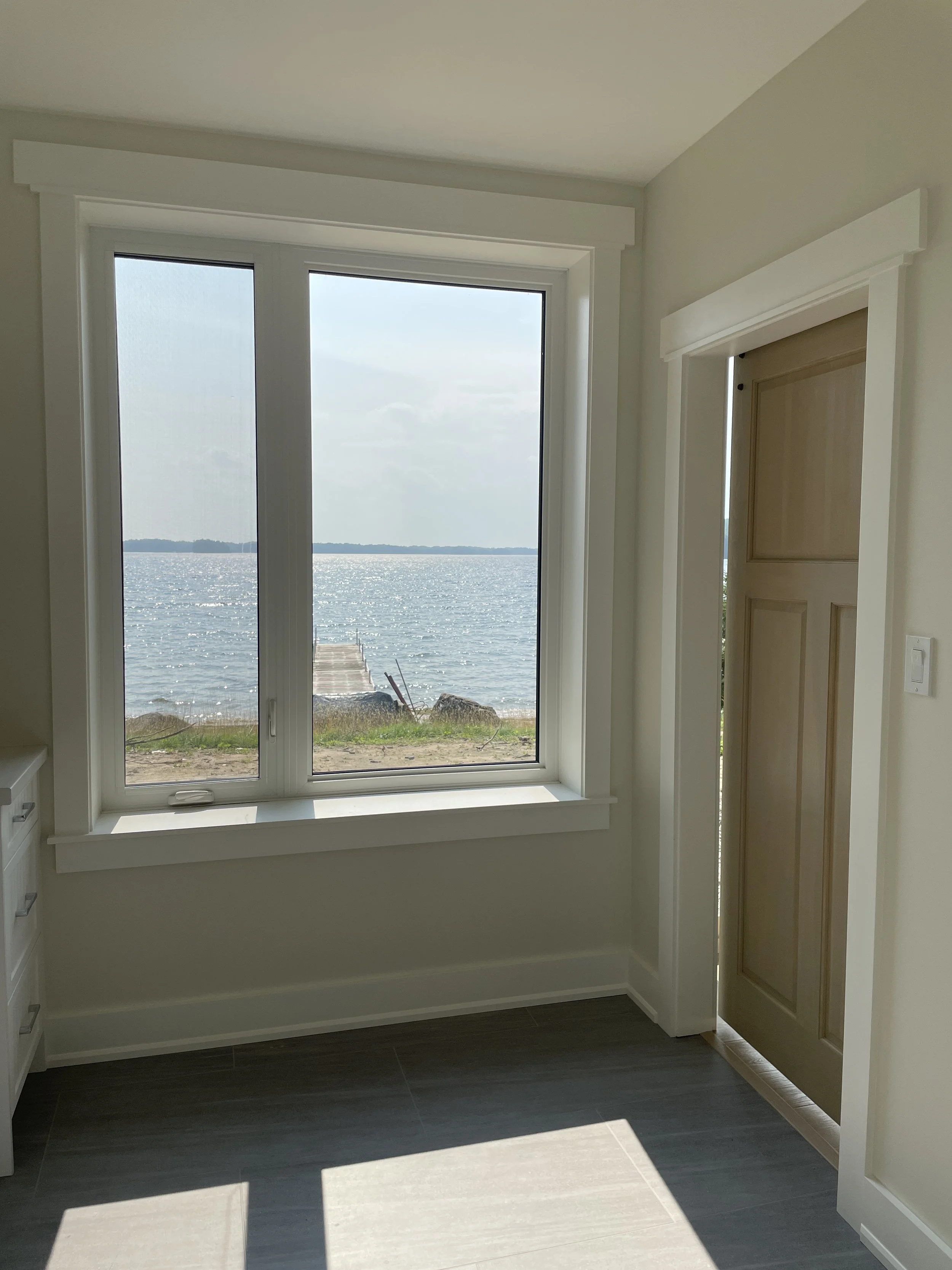 View of a lake through a large window with a sliding mechanism, in a bright room with light-colored walls and dark flooring.