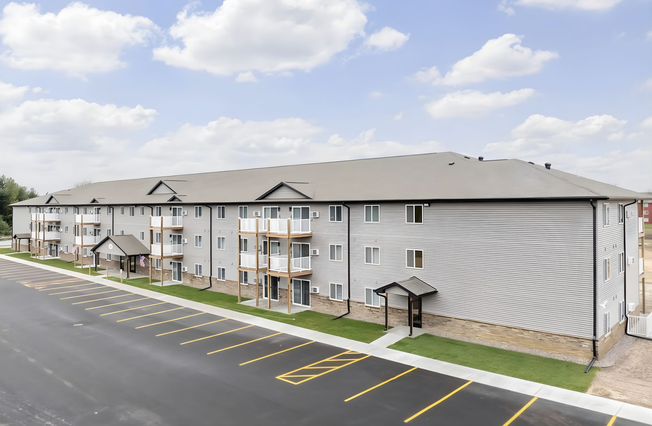 Living room with a large blue sectional sofa, a wooden coffee table, a patterned rug, a flat-screen TV on the wall, and a window with blinds allowing natural light in.