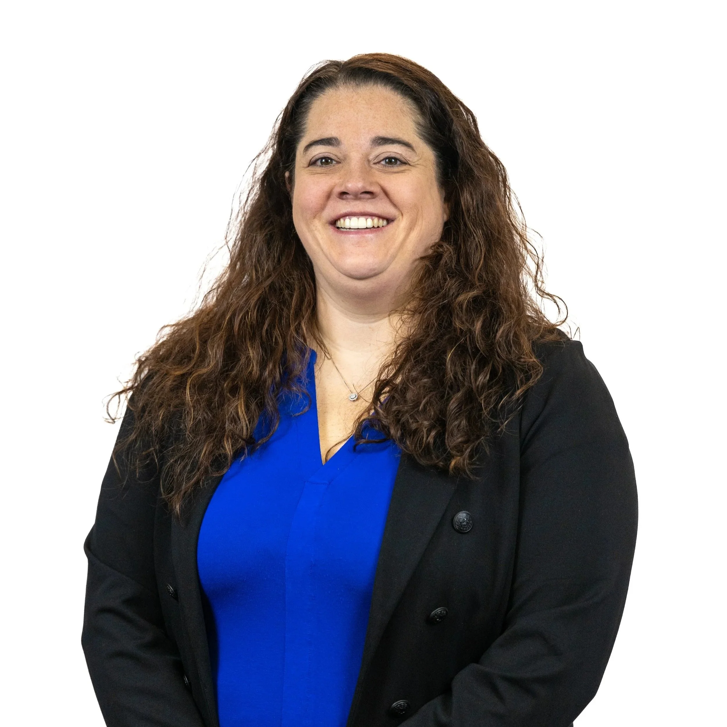 A woman with long curly brown hair smiling, wearing a royal blue blouse and black blazer, standing against a white background.