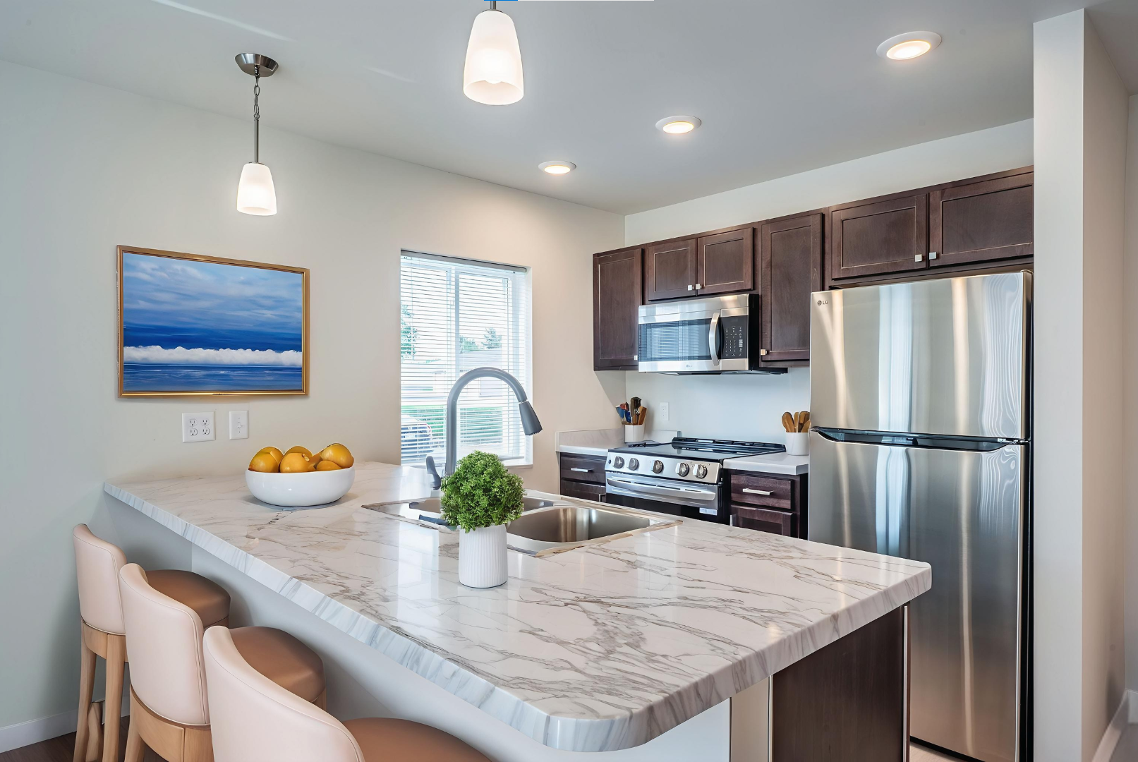 Modern kitchen with marble island, dark wooden cabinets, stainless steel refrigerator, microwave, stove, and hanging lights, with window and decorative items.