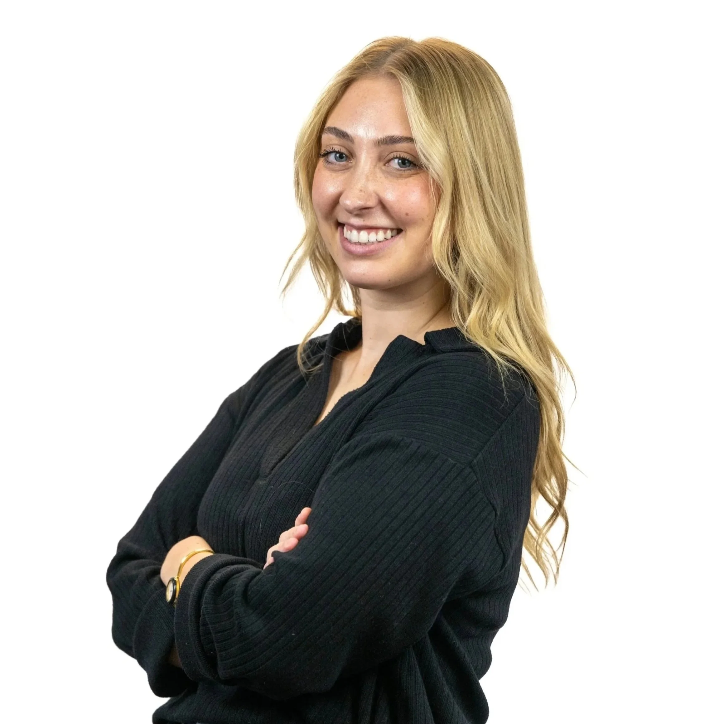 Portrait of a young woman with blonde hair, smiling, wearing a black sweater, arms crossed, against a white background.