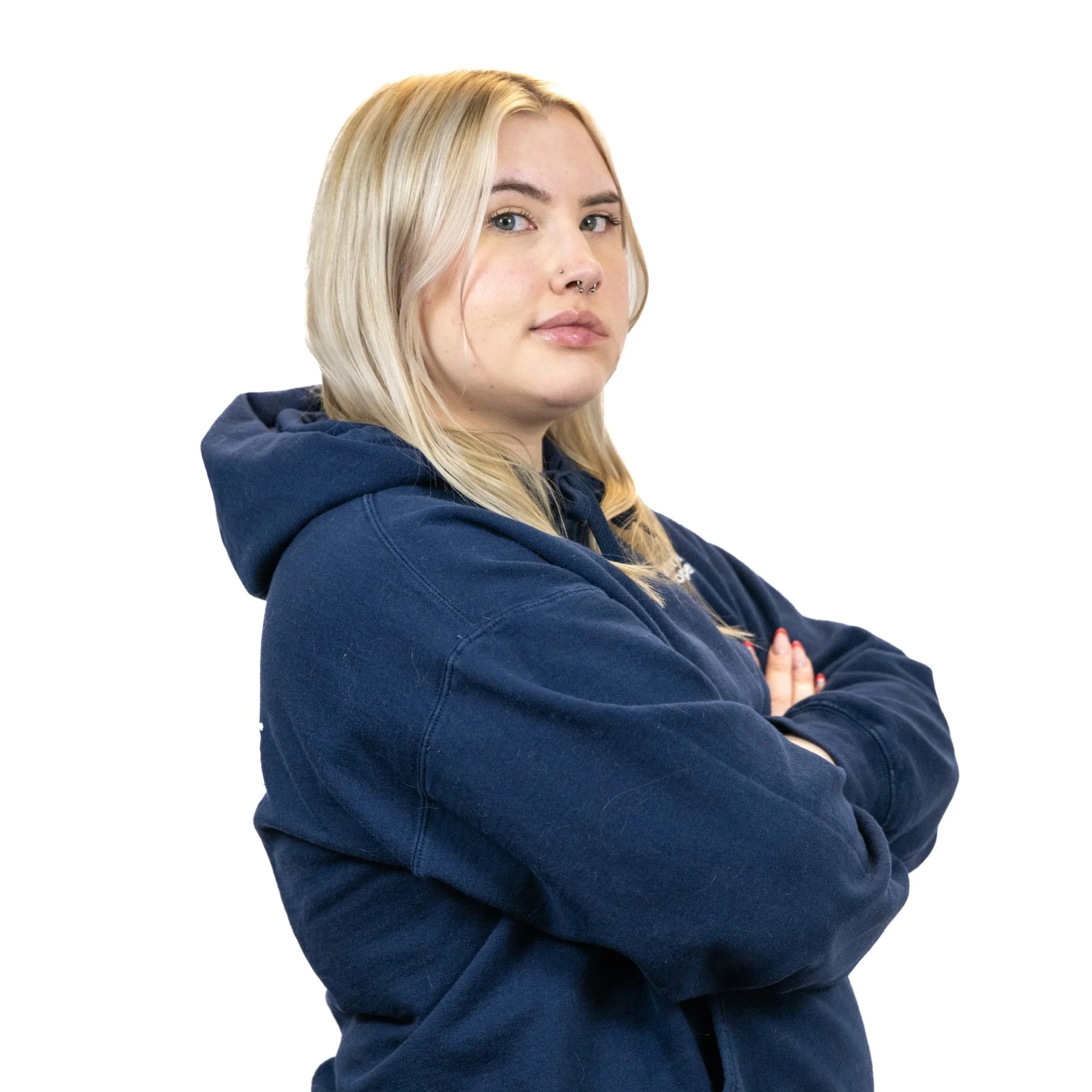 A young woman with blonde hair and fair skin wearing a navy blue hoodie standing with arms crossed against a white background.