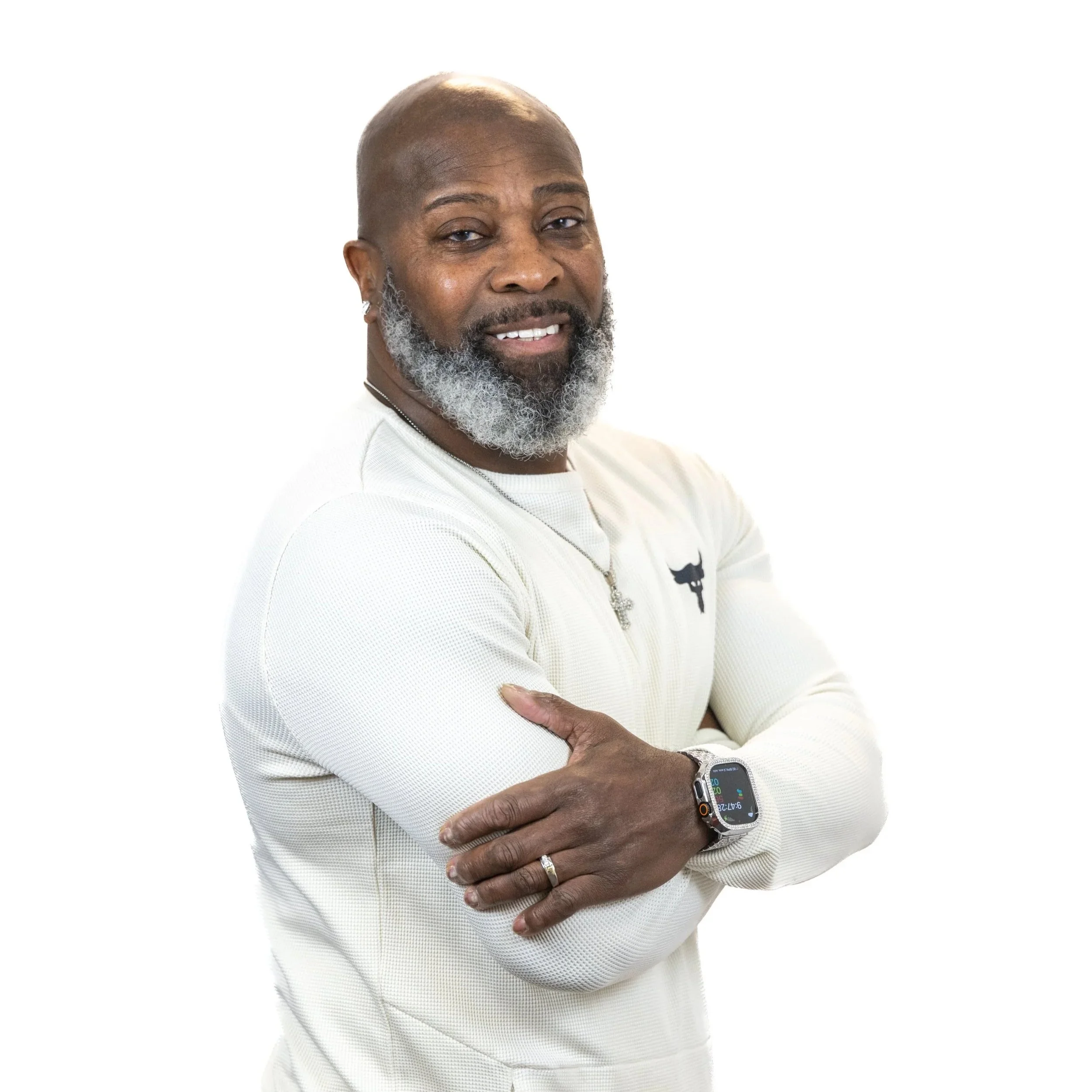 A smiling middle-aged man with a gray beard, wearing a white long-sleeve shirt, sporting a smartwatch, and standing against a plain white background.