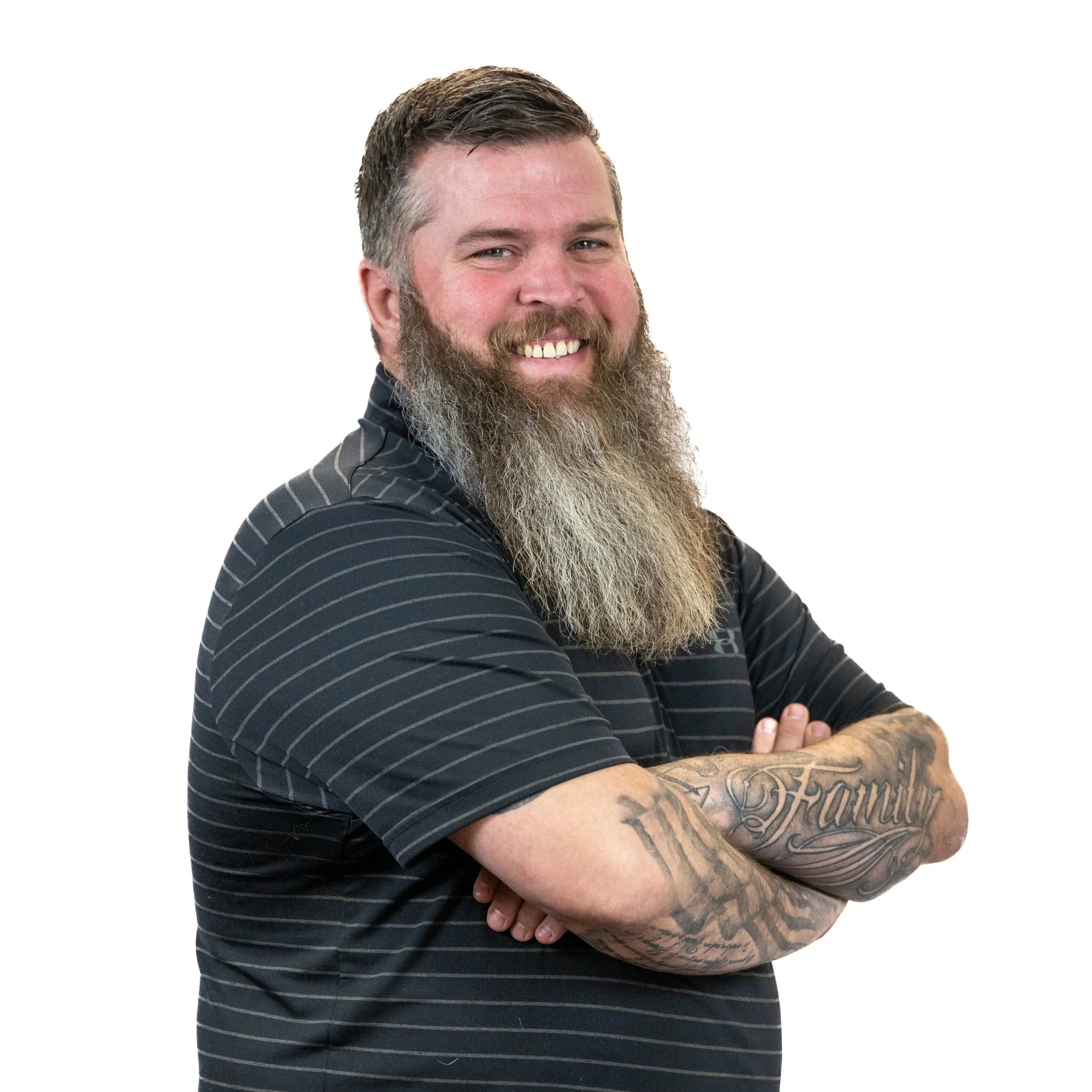A man with a beard and tattoos wearing a black striped polo shirt, smiling and crossing his arms.