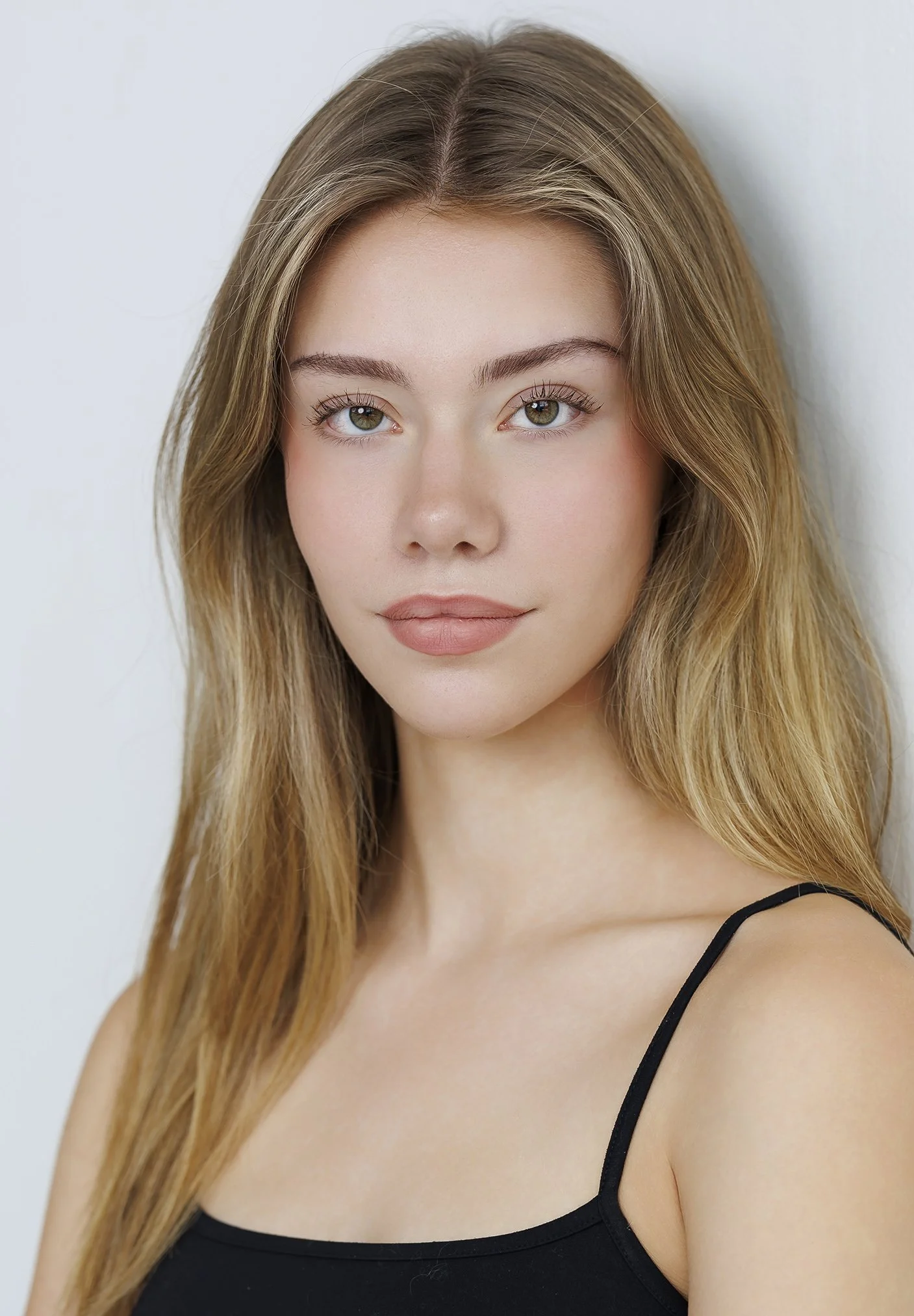 A young woman with long, wavy blonde hair and light makeup looking at the camera against a plain white background.