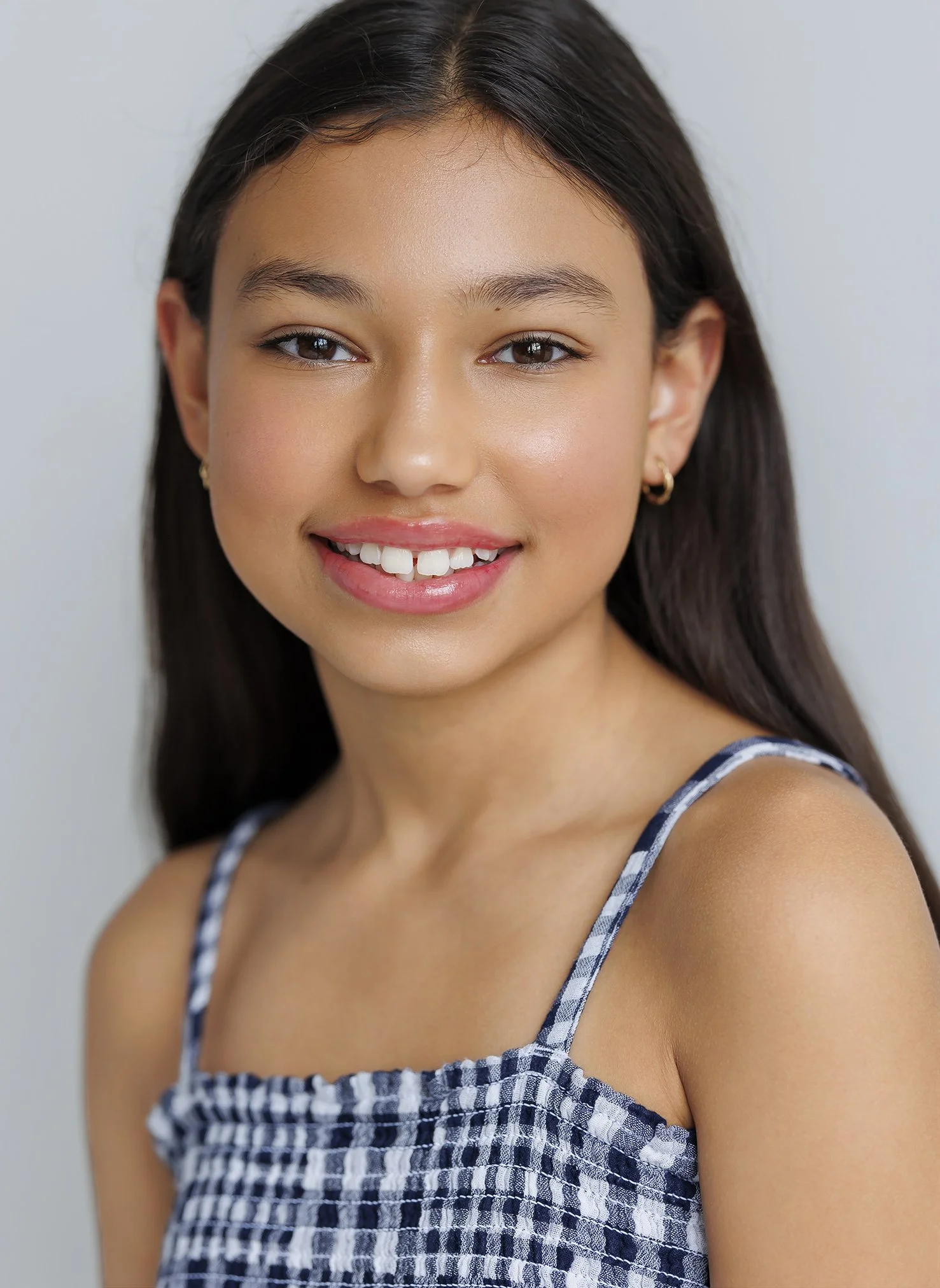 Close-up portrait of a young woman with long dark hair, smiling and wearing a blue and white checkered sleeveless top.