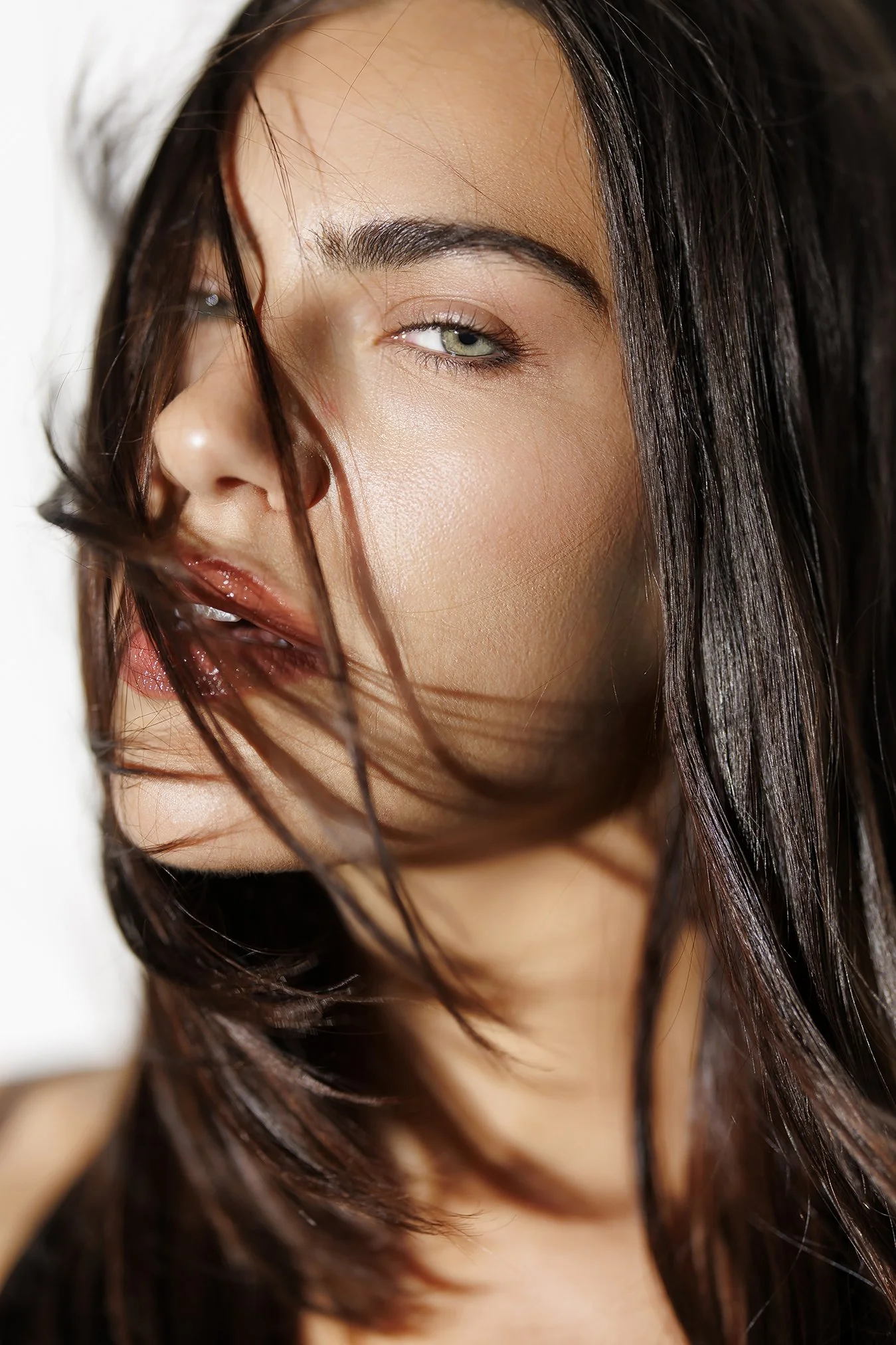 Close-up portrait of a woman with wavy brown hair and green eyes, partially covering her face with her hair.