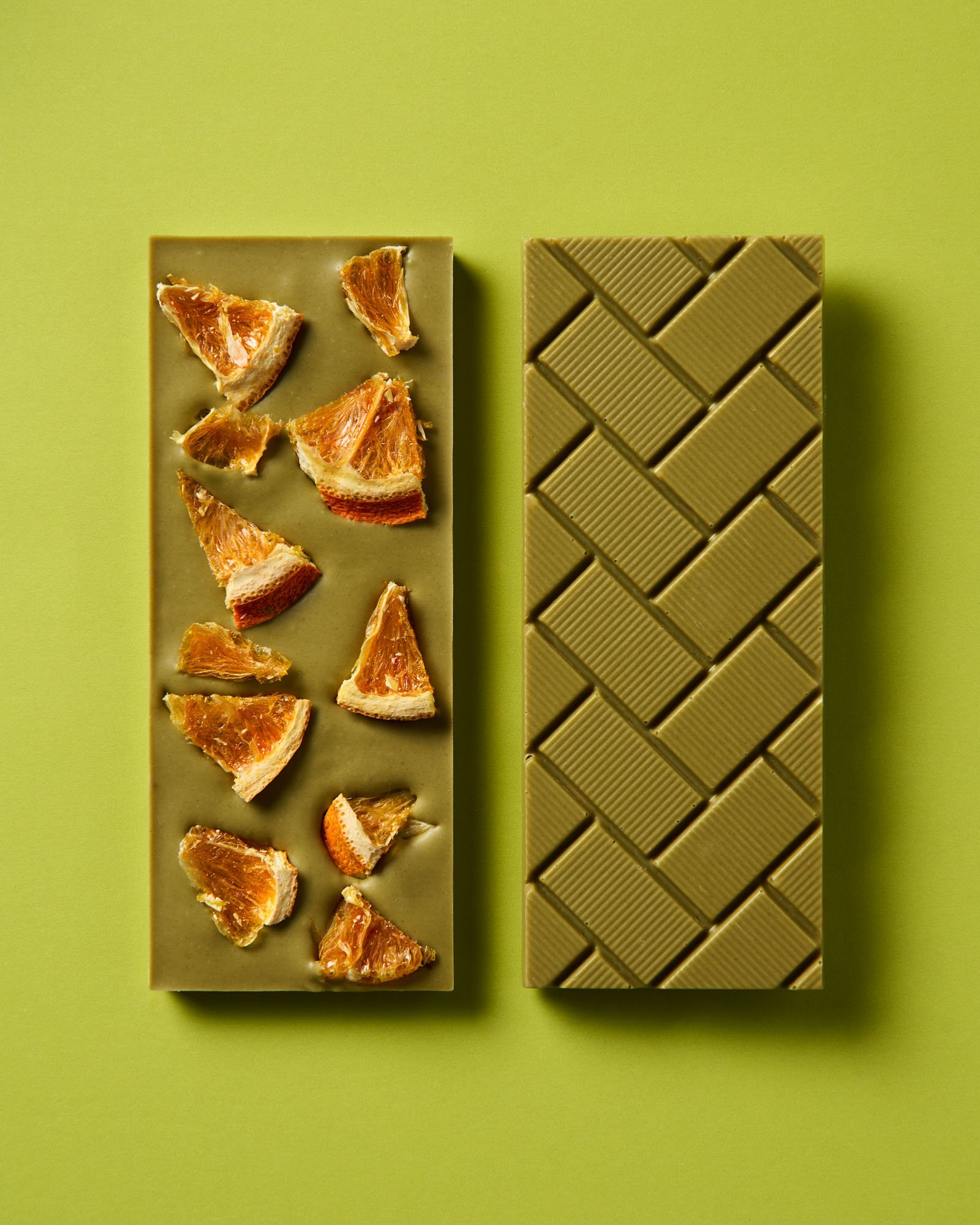 two green chocolate bars next to each other. One is flipped on its back and topped with dried orange slices. The other is face up showing the break-lines of the chocolate bar.