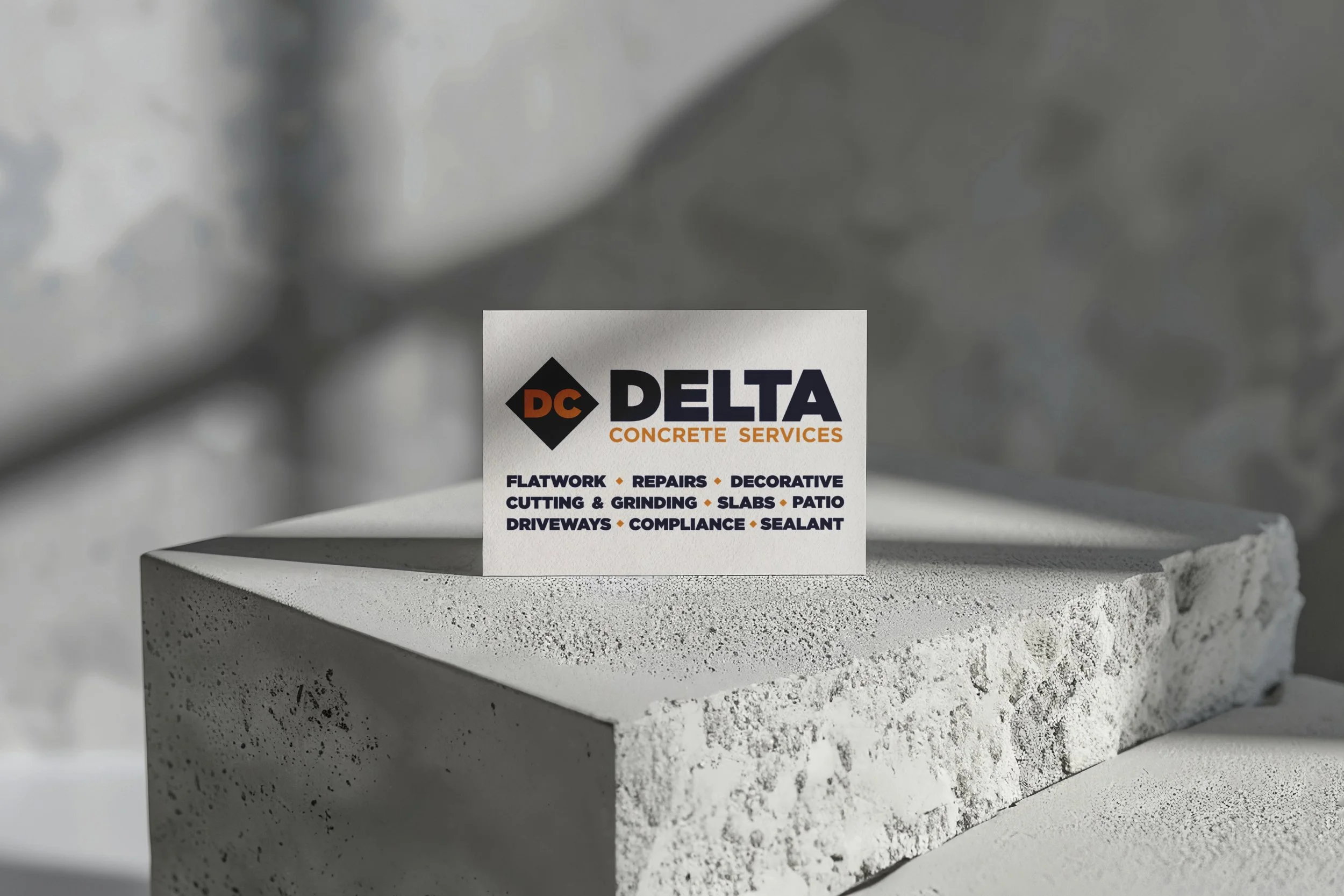 Business card for Delta Concrete Services on a textured concrete surface, highlighting services like flatwork, cutting, grinding, and driveways.