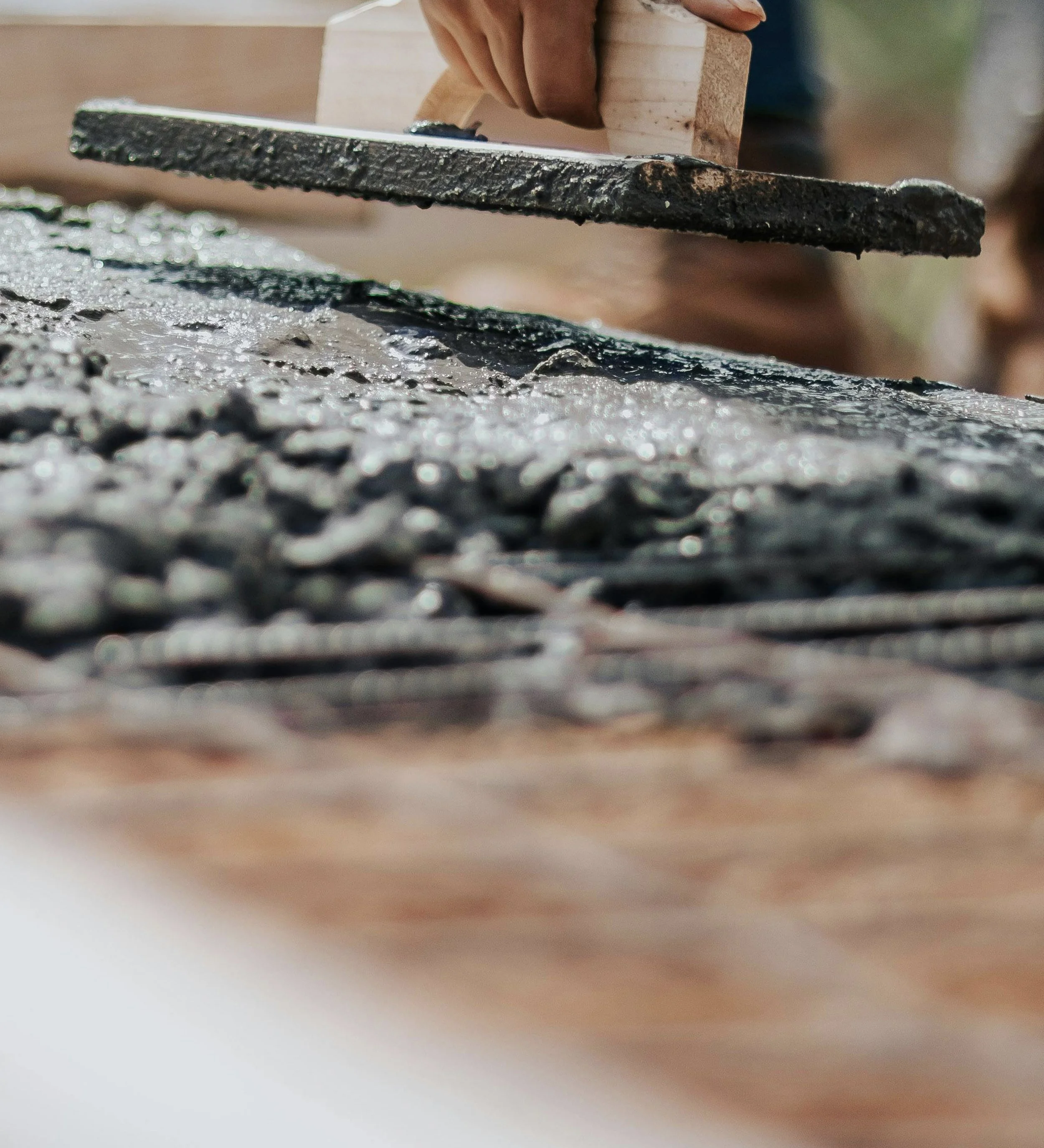 Close-up of a hand smoothing wet concrete with a trowel on a construction site.