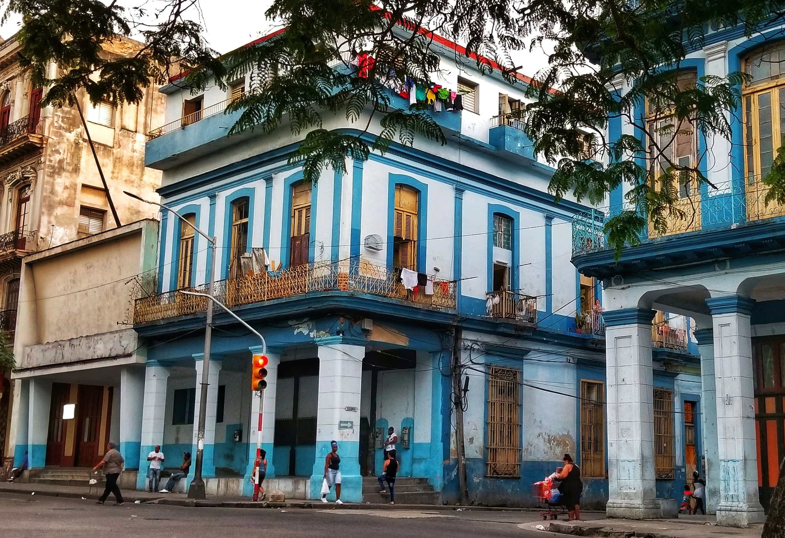 Street corner with a blue and white building, several people walking, and a traffic light showing red.