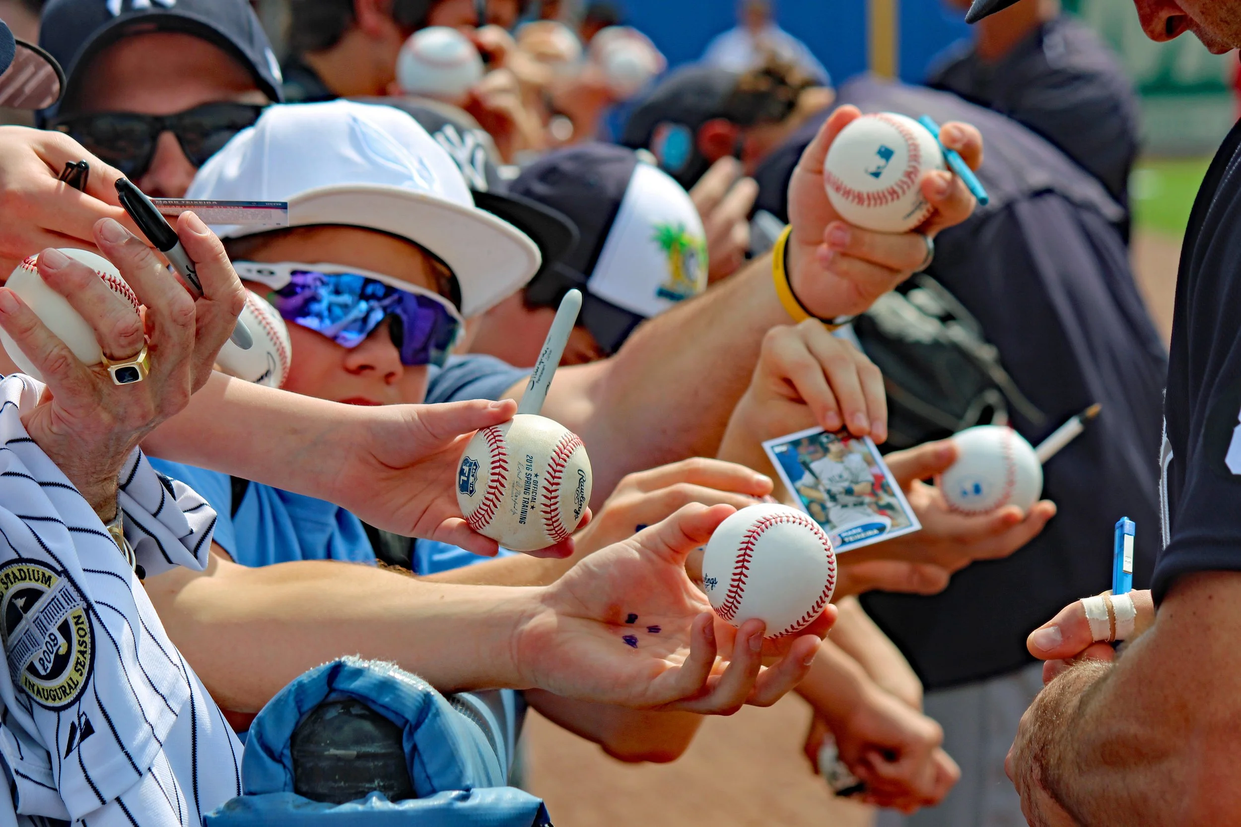 People signing autographs and holding baseballs, likely at a sports event or fan meet-and-greet.