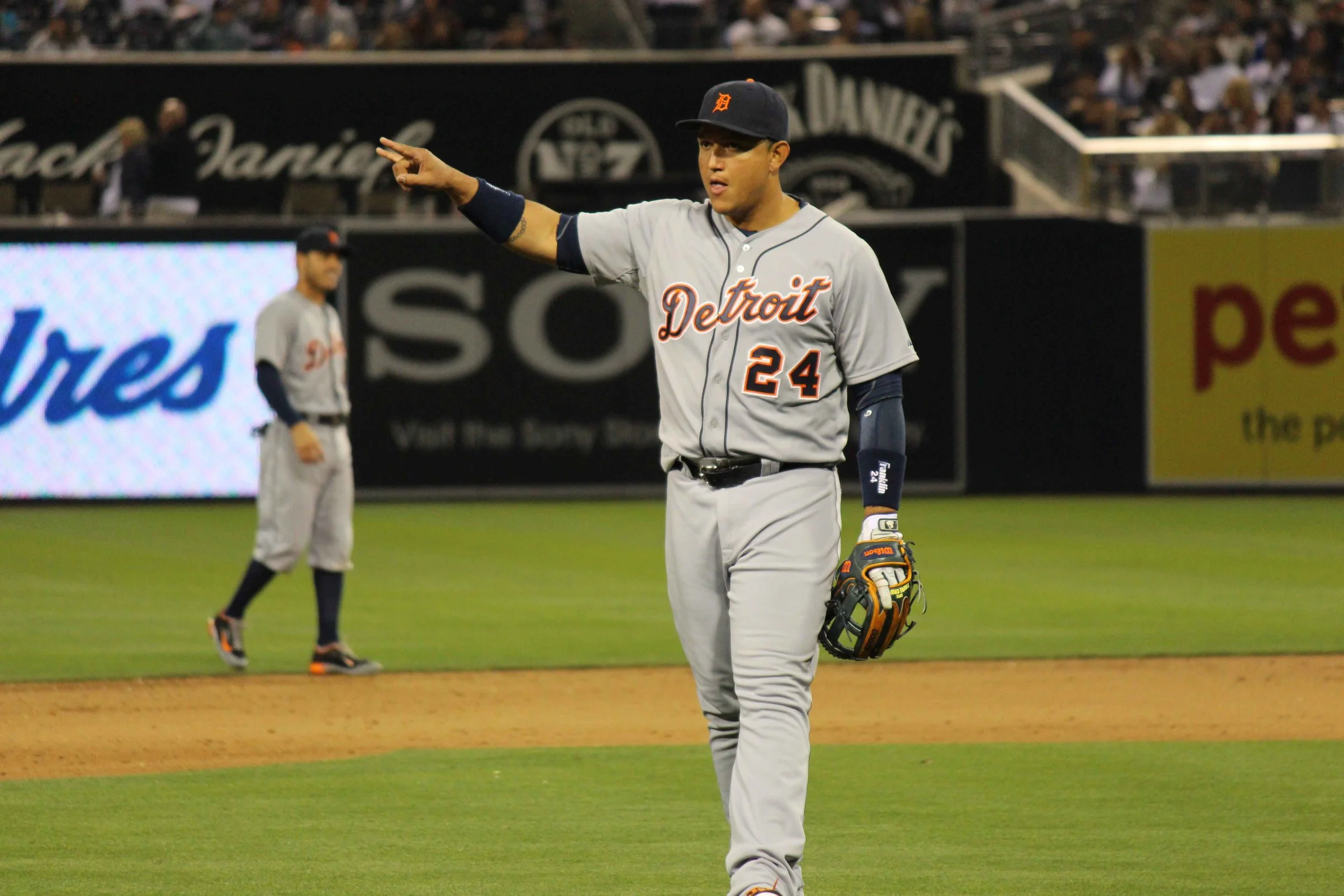 A baseball player from the Detroit team pointing during a game, with another player and fans in the background.