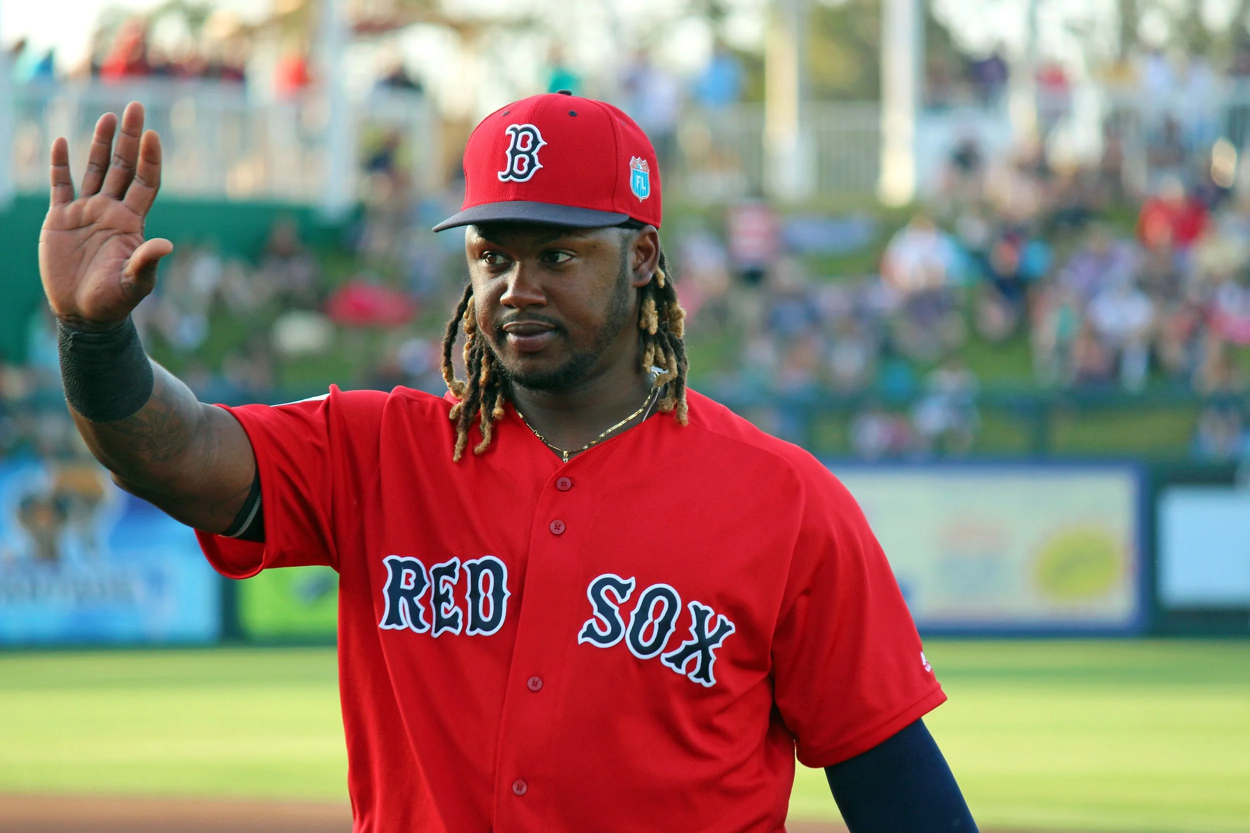 A baseball player in a red uniform with a red cap waving with his right hand on a baseball field during daytime.